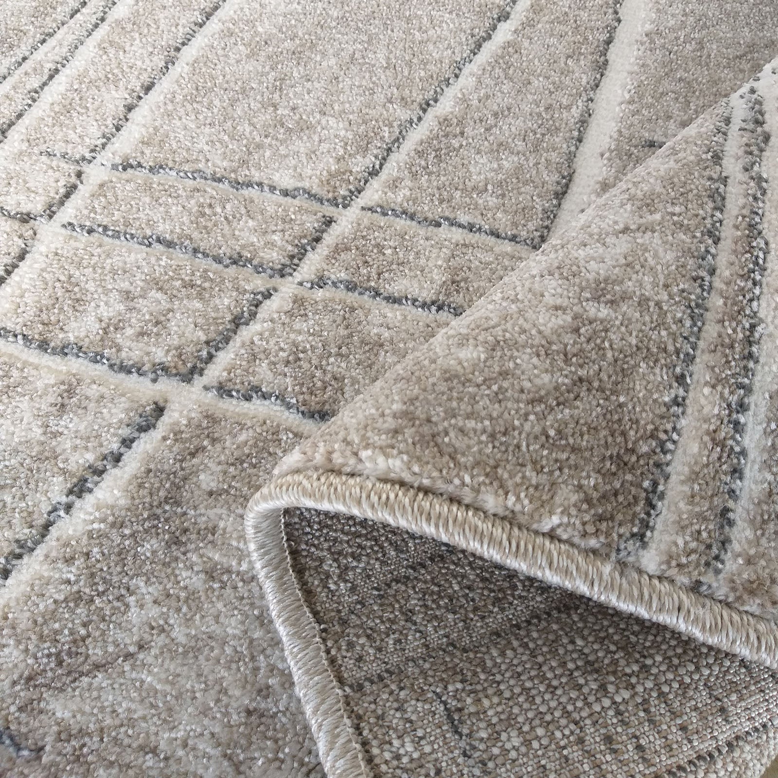 Tapis beige clair à poil long avec un motif géométrique de lignes grises foncées, un coin est roulé