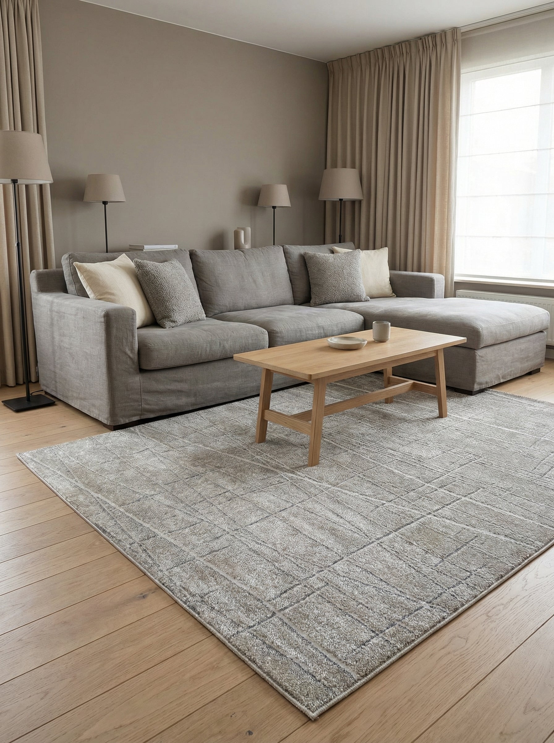 Tapis rectangulaire gris-beige aux motifs géométriques abstraits en relief, formant des carrés et des lignes, dans un salon
