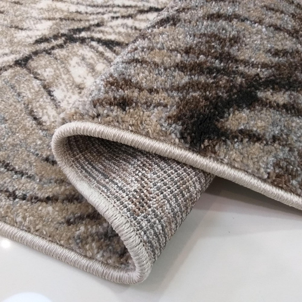 Tapis doux aux tons beiges, marrons et gris avec des motifs abstraits contrastés, dont le bord est ourlé et roulé