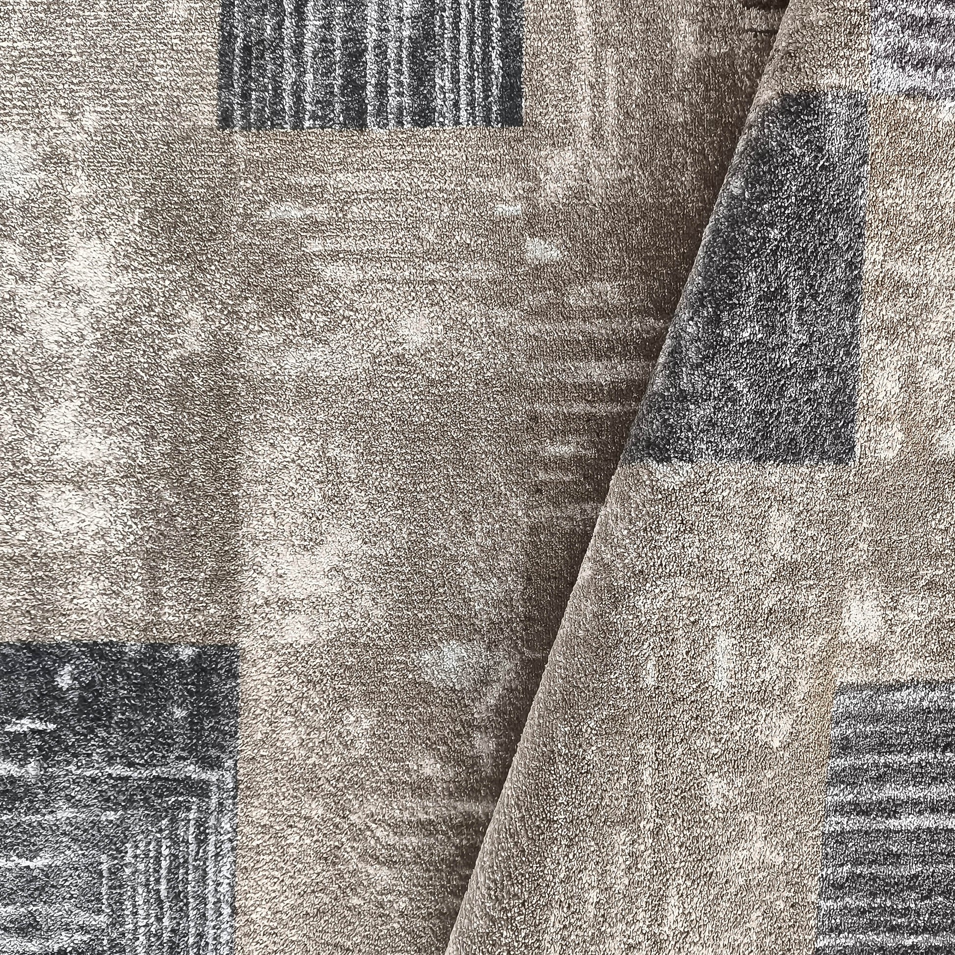 Tapis moelleux aux tons beiges et gris foncé, avec des motifs abstraits et une texture bouclée, plié au centre
