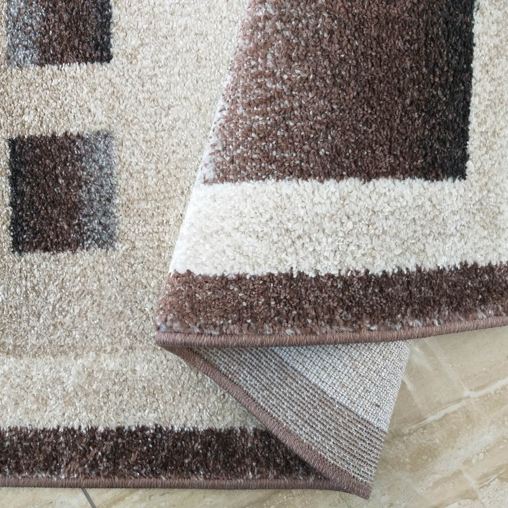 Tapis textile bouclé marron, beige et crème, à motifs géométriques de carrés et rayures. Une partie est repliée
