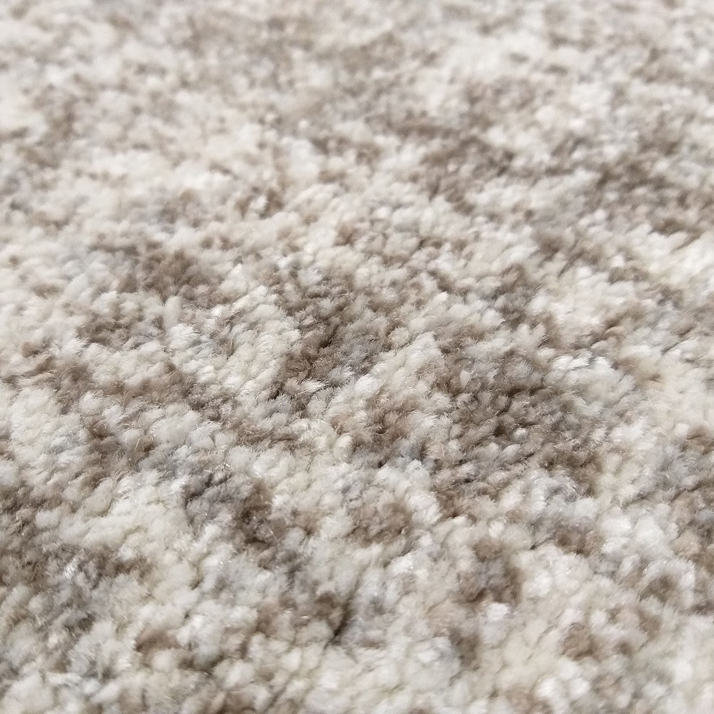 Gros plan sur un tapis texturé à poils longs, aux motifs irréguliers mêlant des nuances de crème et de brun clair