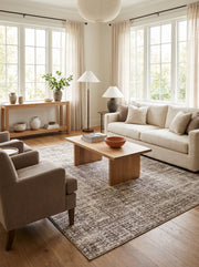 Tapis rectangulaire aux motifs abstraits texturés marron et beige clair, posé sur un parquet en bois dans un salon lumineux