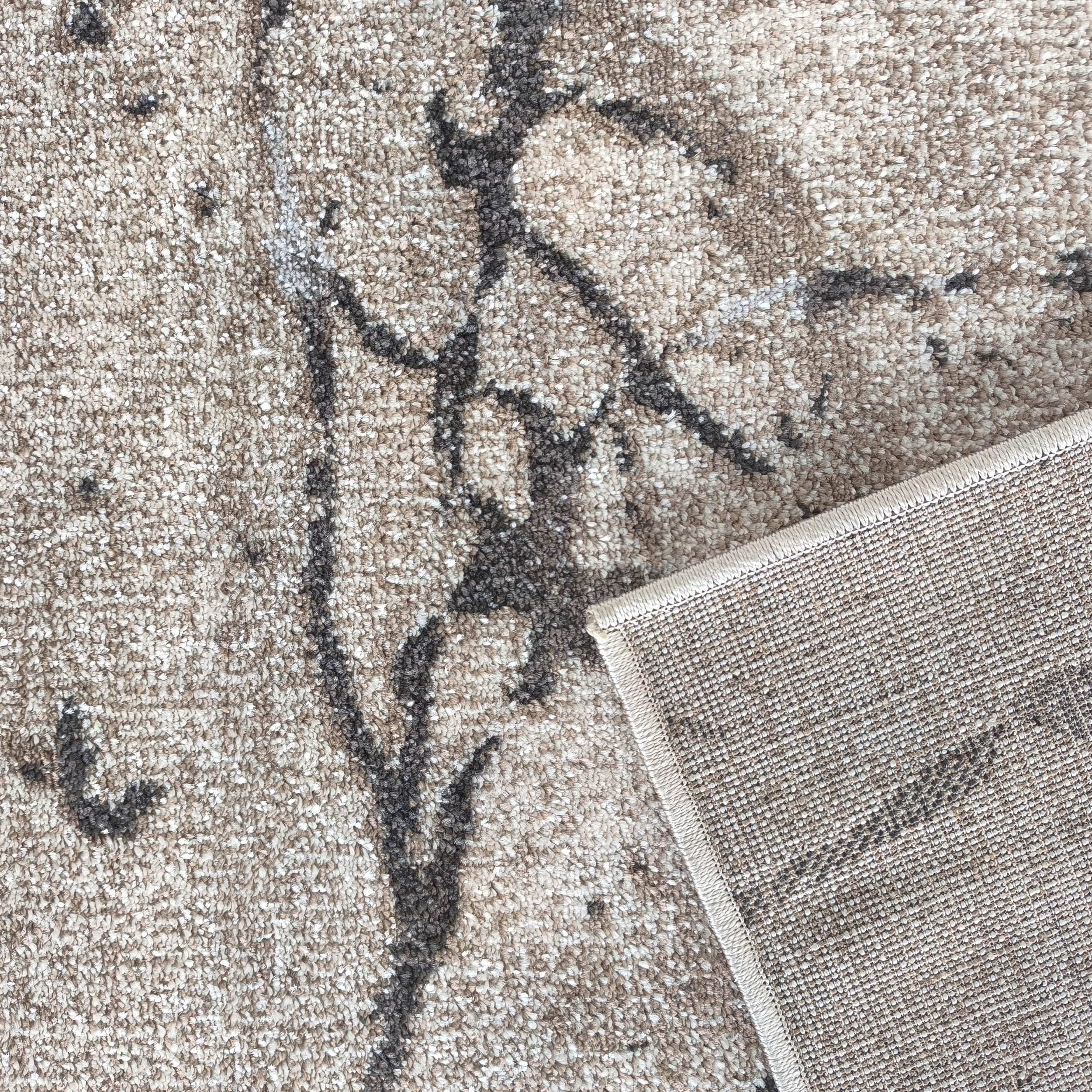 Tapis beige clair et crème à l'aspect bouclé avec des motifs abstraits sombres. Le revers tissé est visible dans un coin