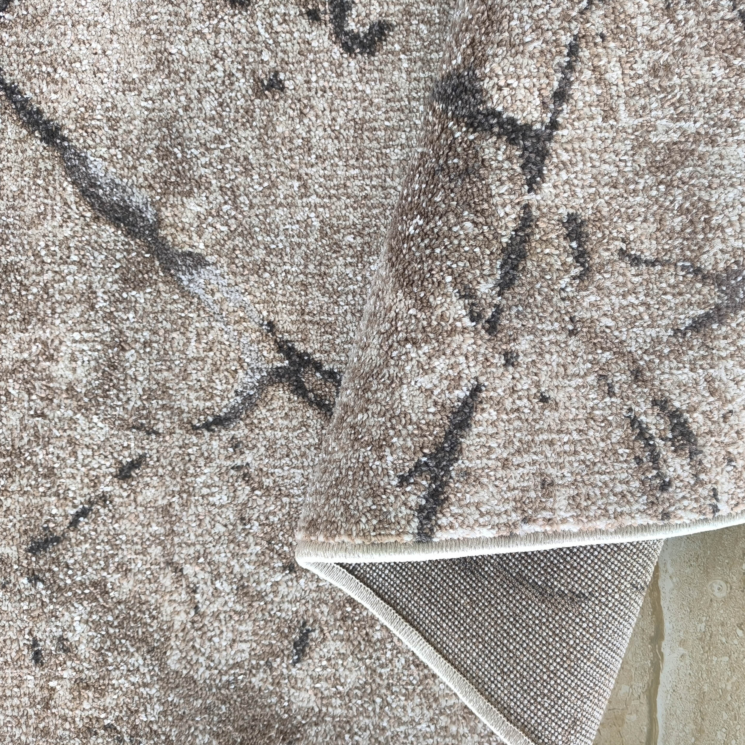 Tapis texturé beige et crème aux motifs abstraits foncés, partiellement enroulé sur le côté droit
