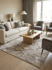 Tapis rectangulaire beige et marron aux motifs abstraits sombres évoquant des fissures, posé sur parquet clair dans un salon