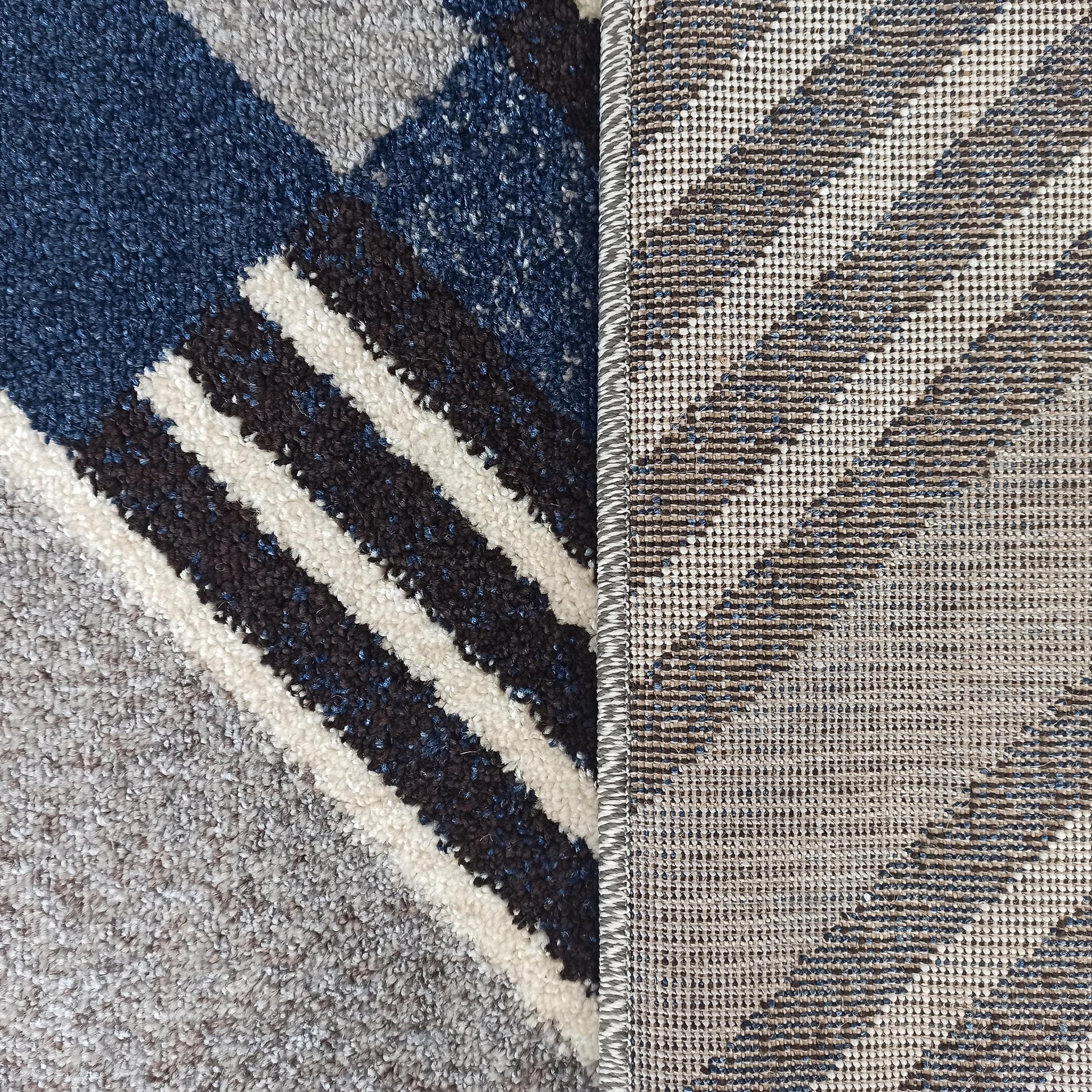 Tapis à poils longs aux motifs géométriques bleus, gris, noirs et blancs, et son envers tissé à rayures obliques crème et marron avec du bleu