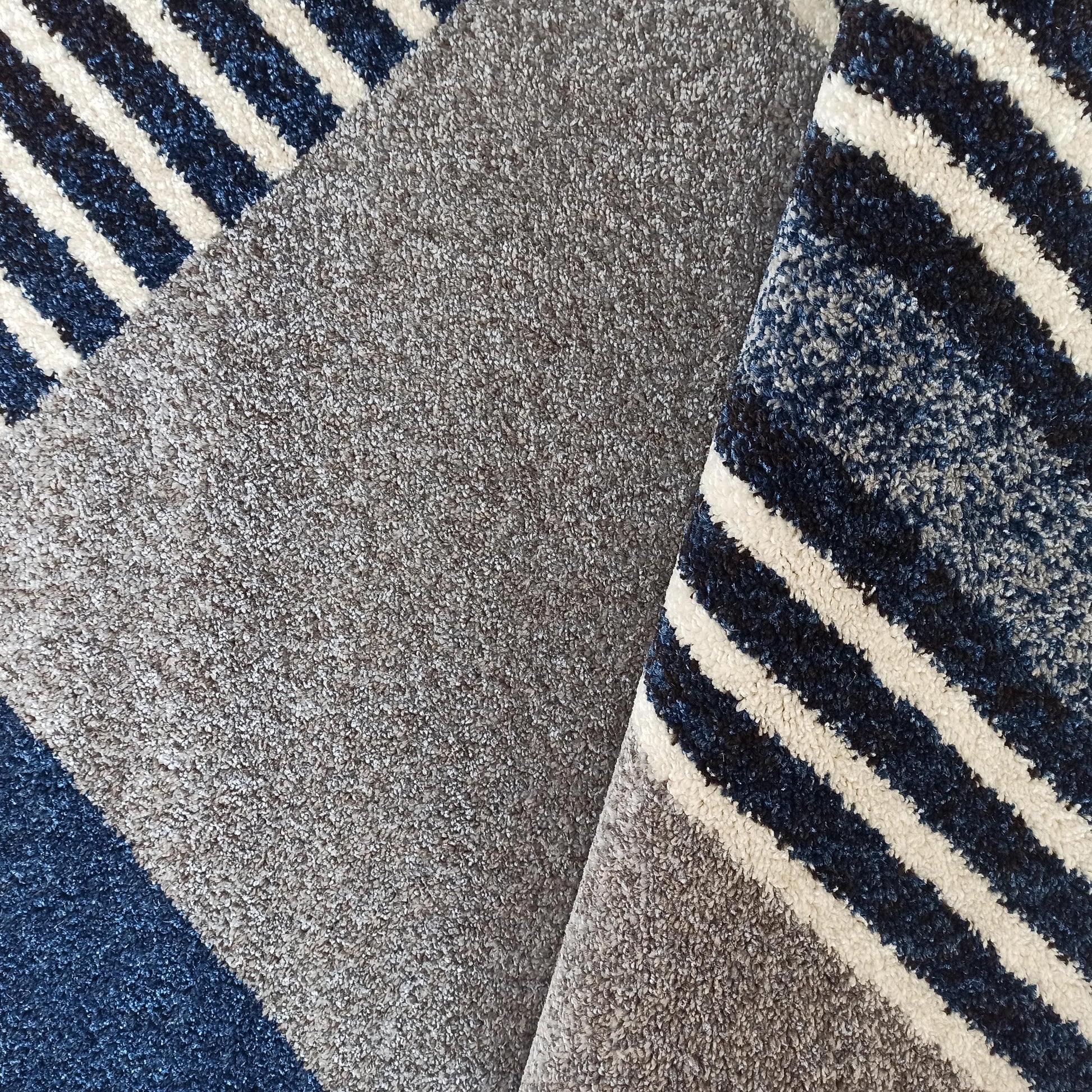 Tapis à poils longs avec des rayures épaisses bleu foncé et blanc cassé, complétées par des zones gris chiné