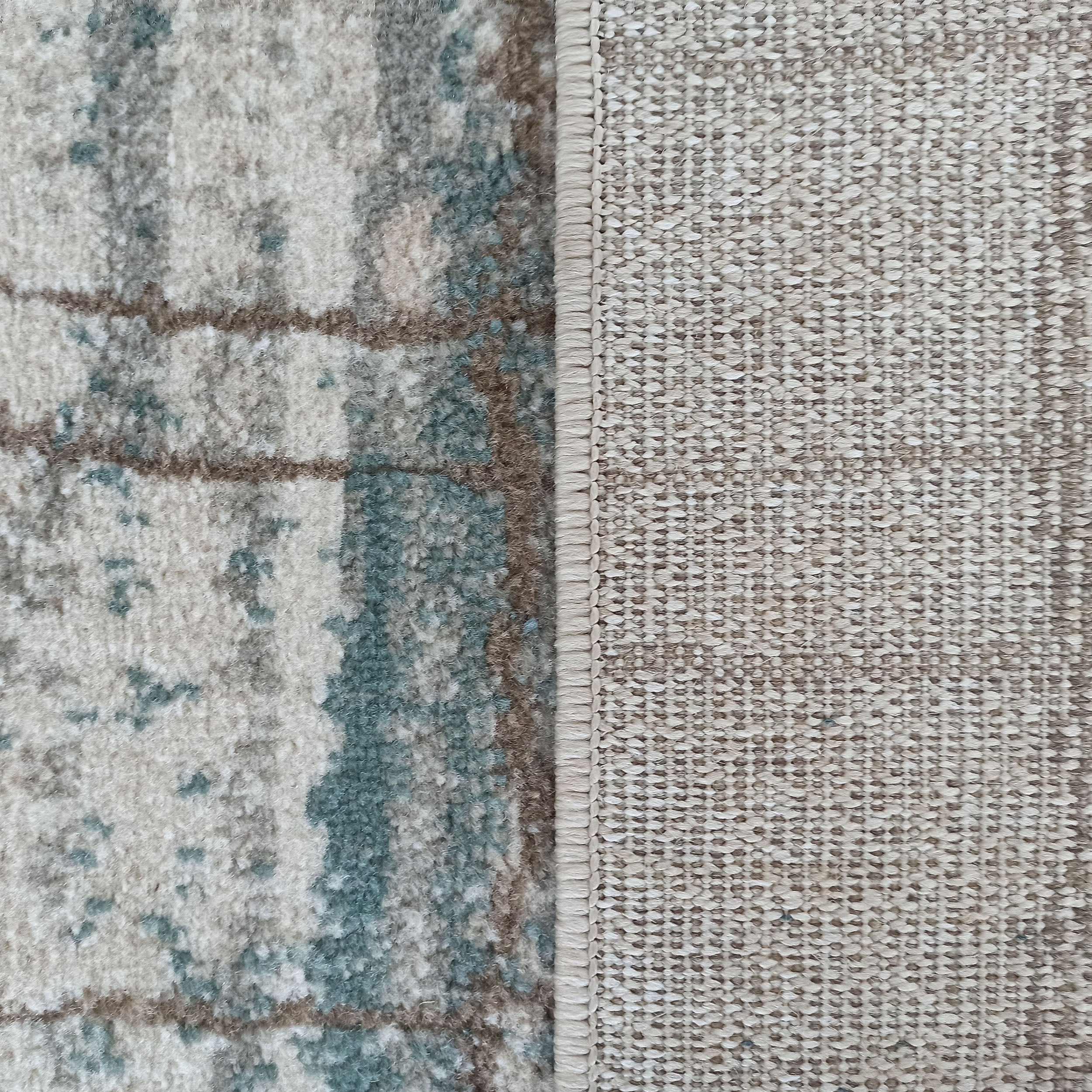 Tapis avec sa surface à texture douce et motifs abstraits beige, bleu-vert et marron, et son revers tissé clair visible sur le côté