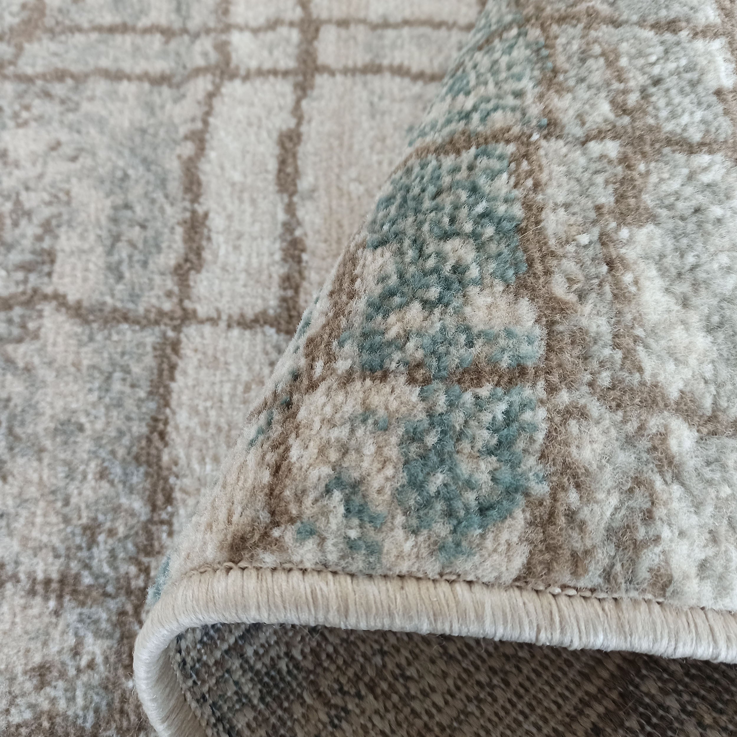 Tapis doux et moelleux aux motifs abstraits géométriques beige, bleu-vert et marron clair, avec un bord roulé