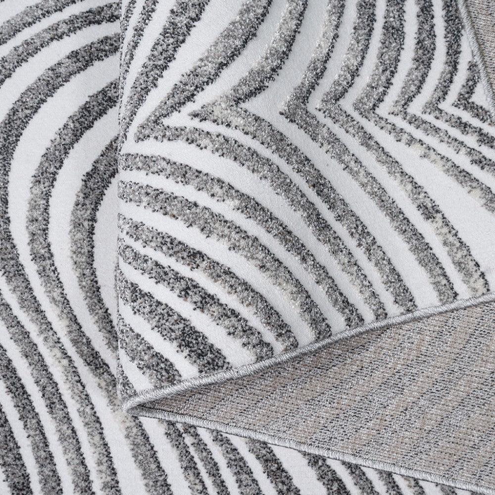 Tapis blanc aux motifs gris texturés formant des vagues et des zigzags, avec le revers tissé visible