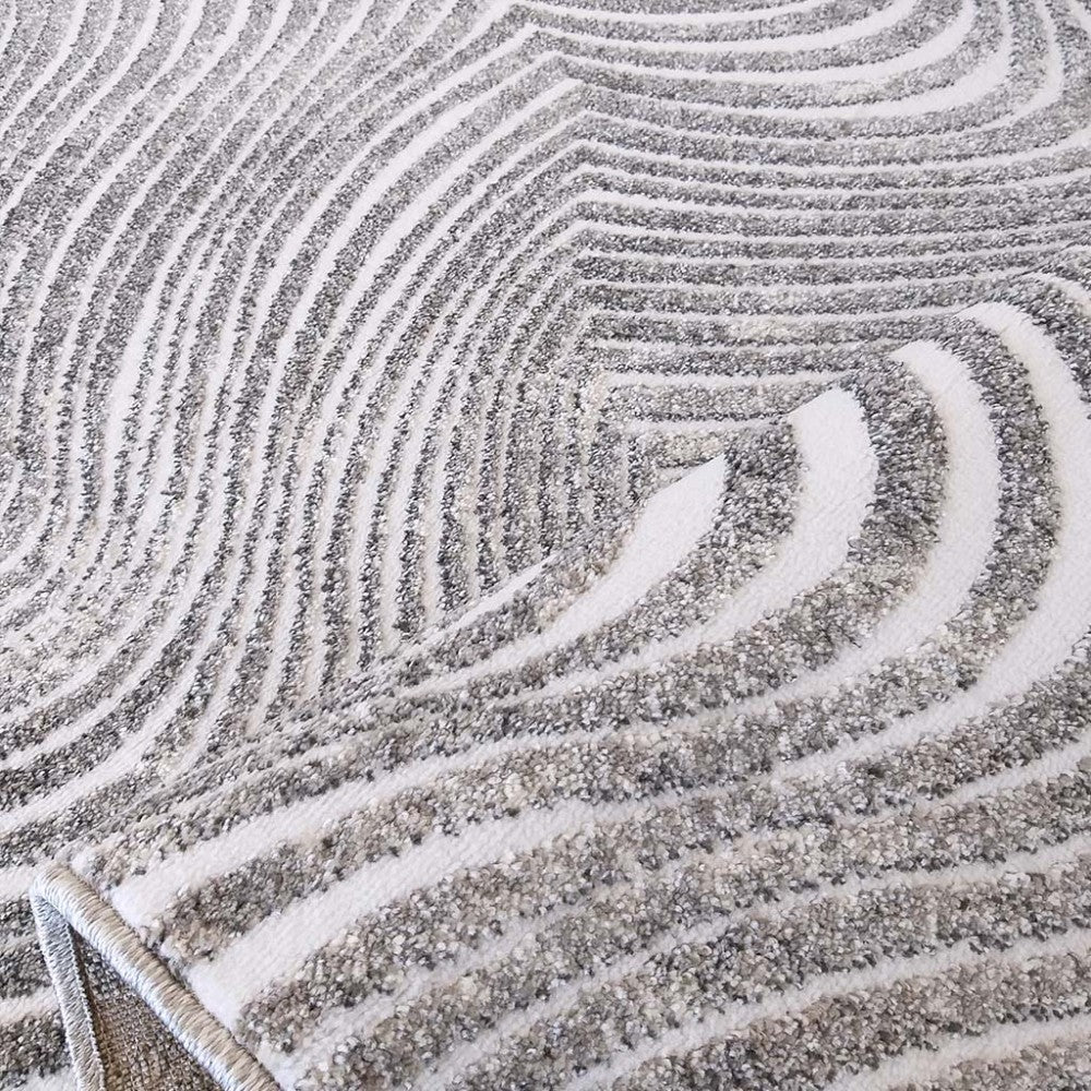 Tapis gris et blanc présentant des motifs de vagues abstraites, avec des zones grises texturées et des lignes blanches lisses