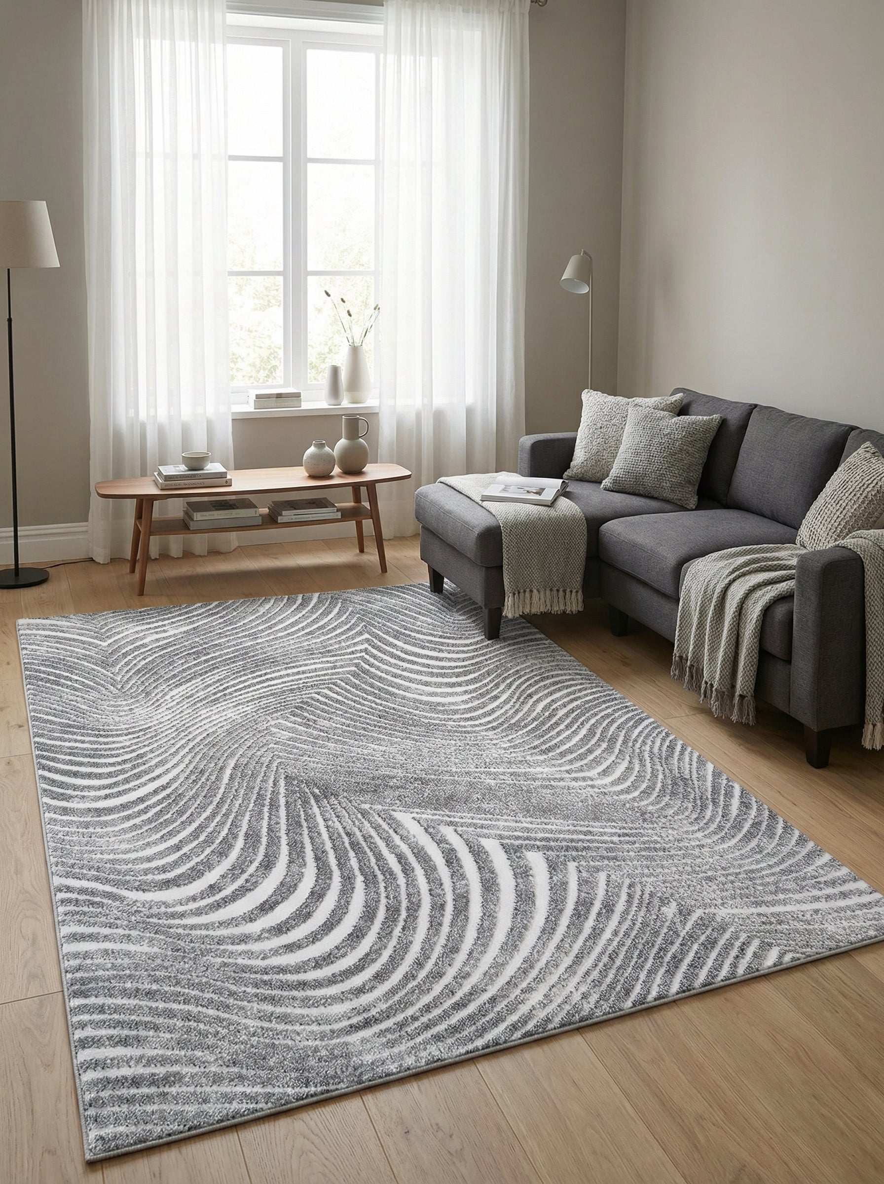 Tapis rectangulaire texturé gris et blanc avec des motifs de vagues abstraites, posé sur un parquet en bois dans un salon lumineux