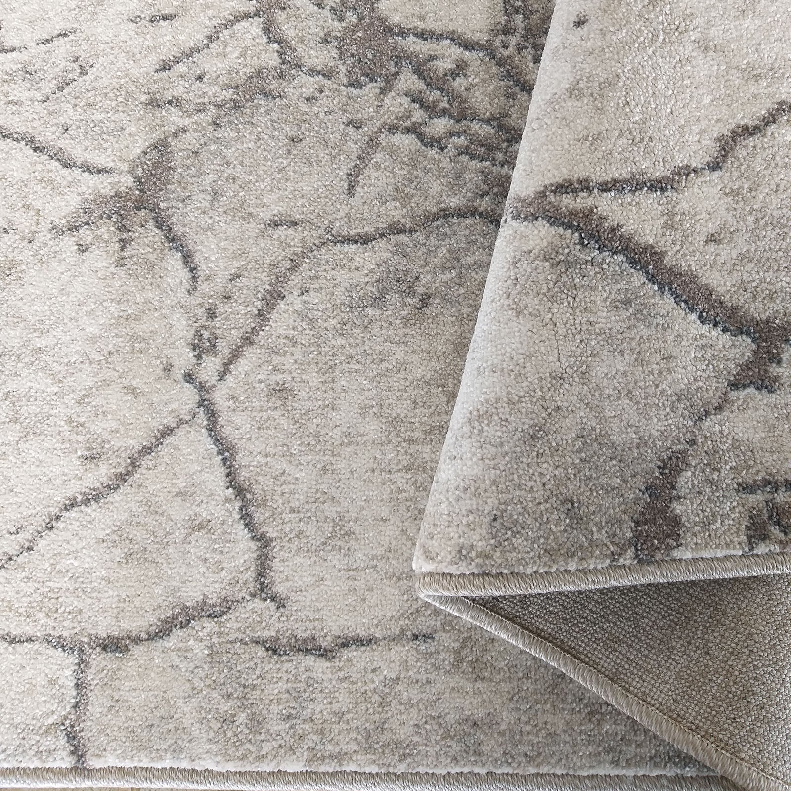 Tapis à poils courts beige sable avec des motifs abstraits brun-gris, une partie est enroulée montrant le revers