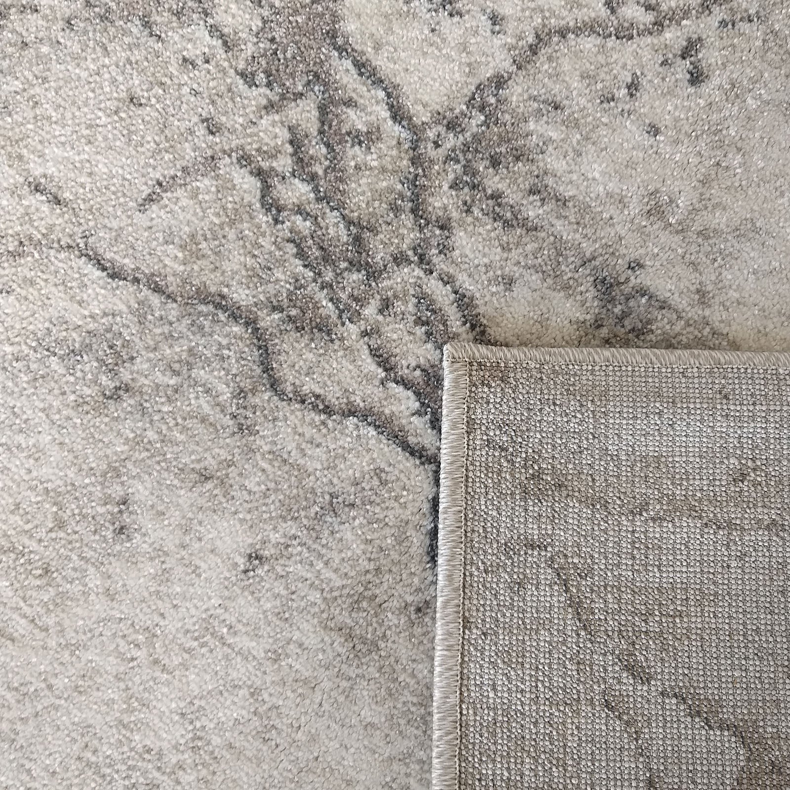 Tapis à poils courts beige et gris avec un motif abstrait marbré. Un coin est relevé montrant le revers tissé