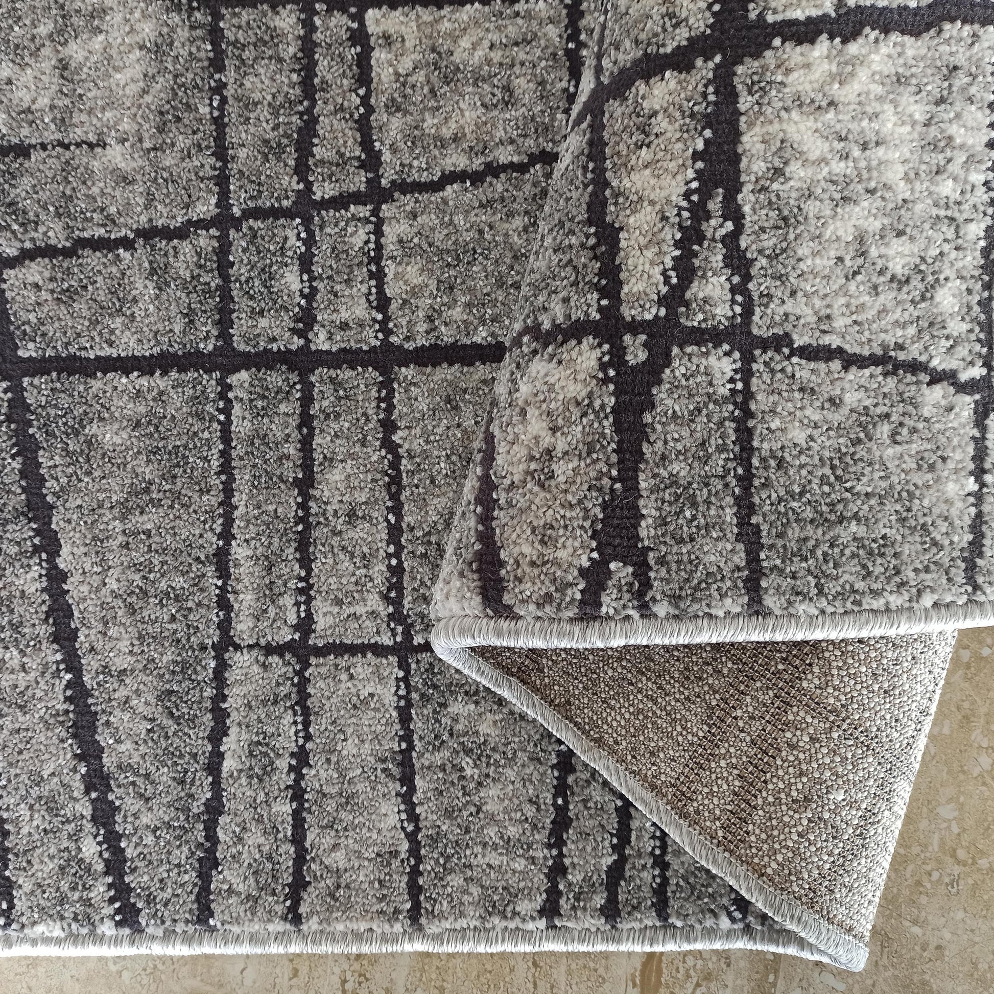 Tapis à poils longs gris clair et foncé, au motif quadrillé irrégulier, dont un coin est relevé