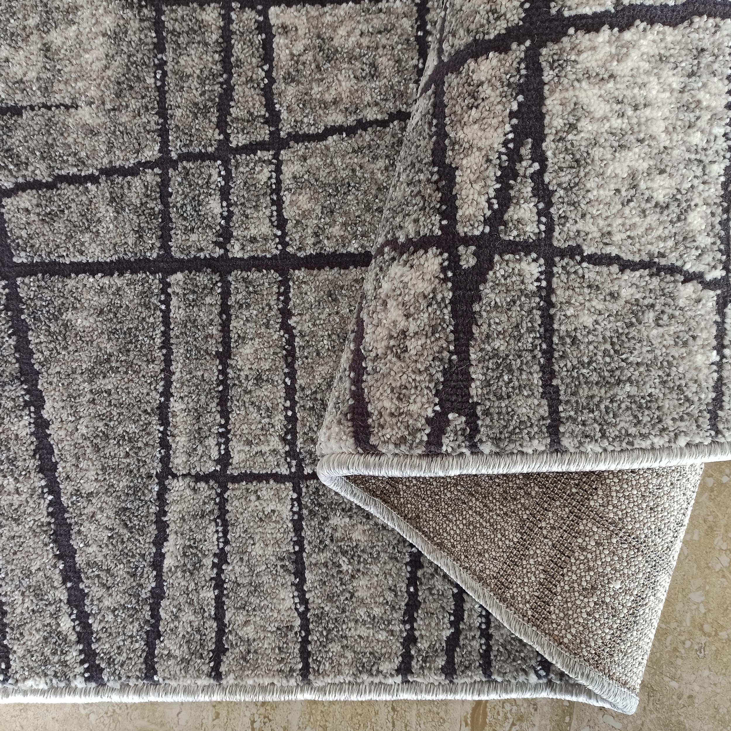 Tapis à poils longs gris clair et foncé, au motif quadrillé irrégulier, dont un coin est relevé