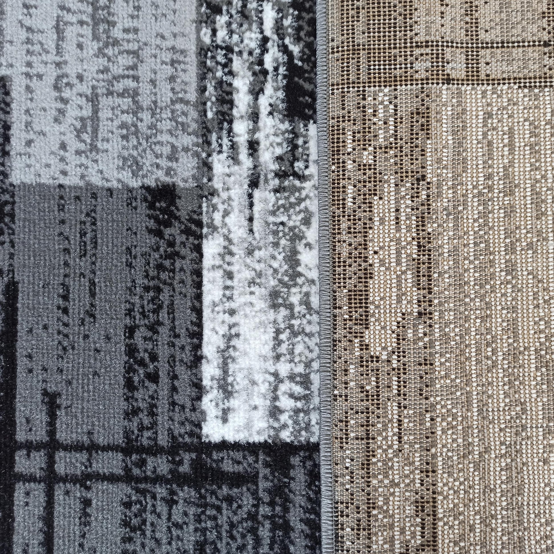 Gros plan d'un tapis, avec le dessus texturé à motif abstrait gris, noir, blanc et le dessous tissé beige et marron