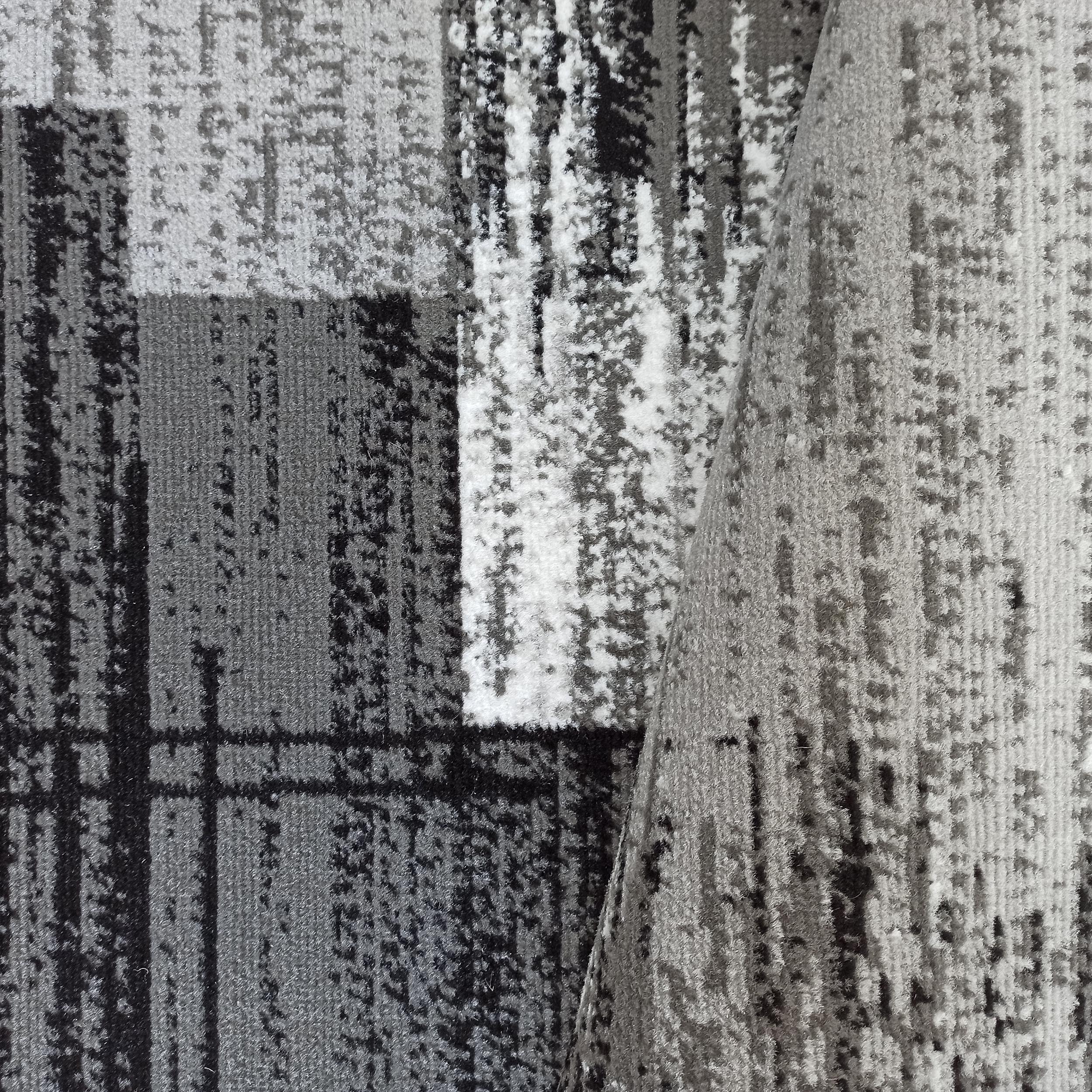 Tapis aux motifs abstraits gris, noirs et blancs, avec une texture visible, partiellement roulé
