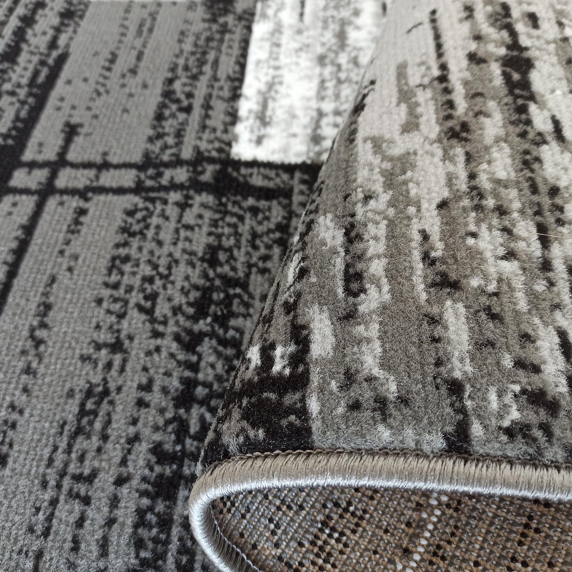 Gros plan sur un tapis aux motifs abstraits gris, noirs et blancs, dont un bord est roulé