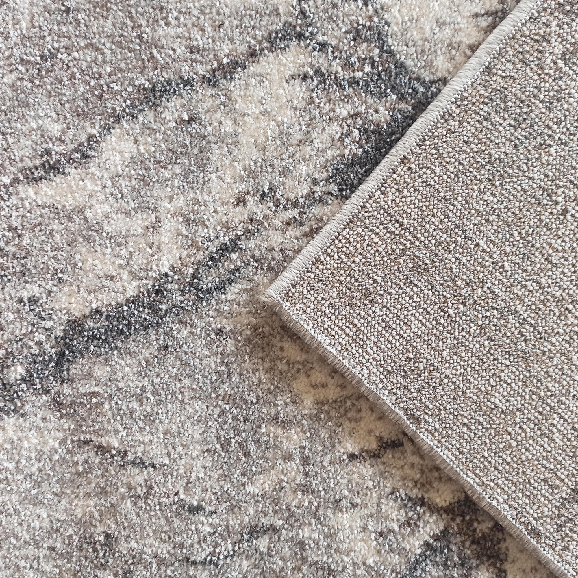 Tapis aux motifs abstraits chinés gris, beige et blanc cassé, avec son envers tissé clair visible