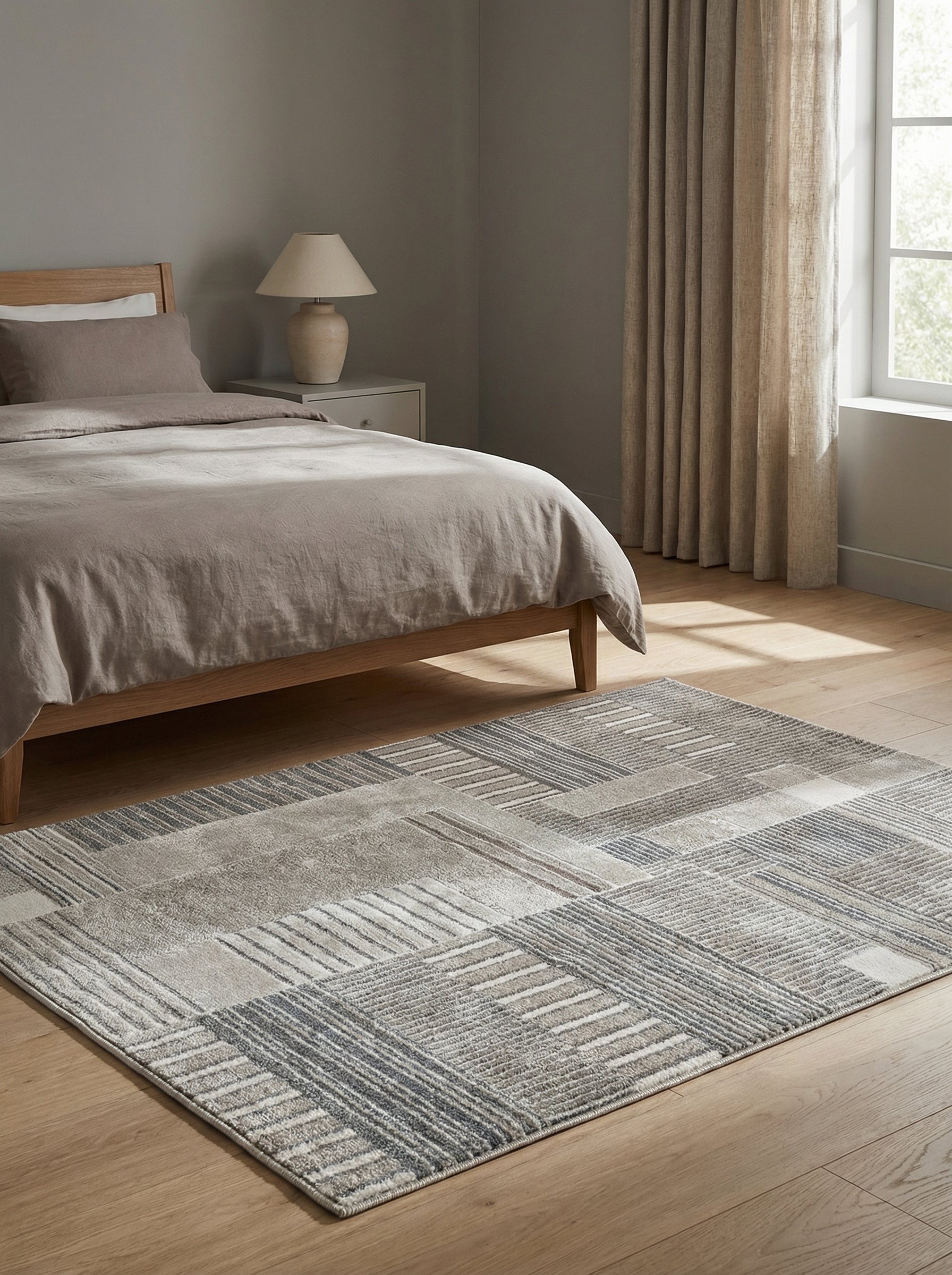 Tapis rectangulaire gris et beige, aux motifs géométriques de blocs et de fines rayures, sur un plancher en bois dans une chambre