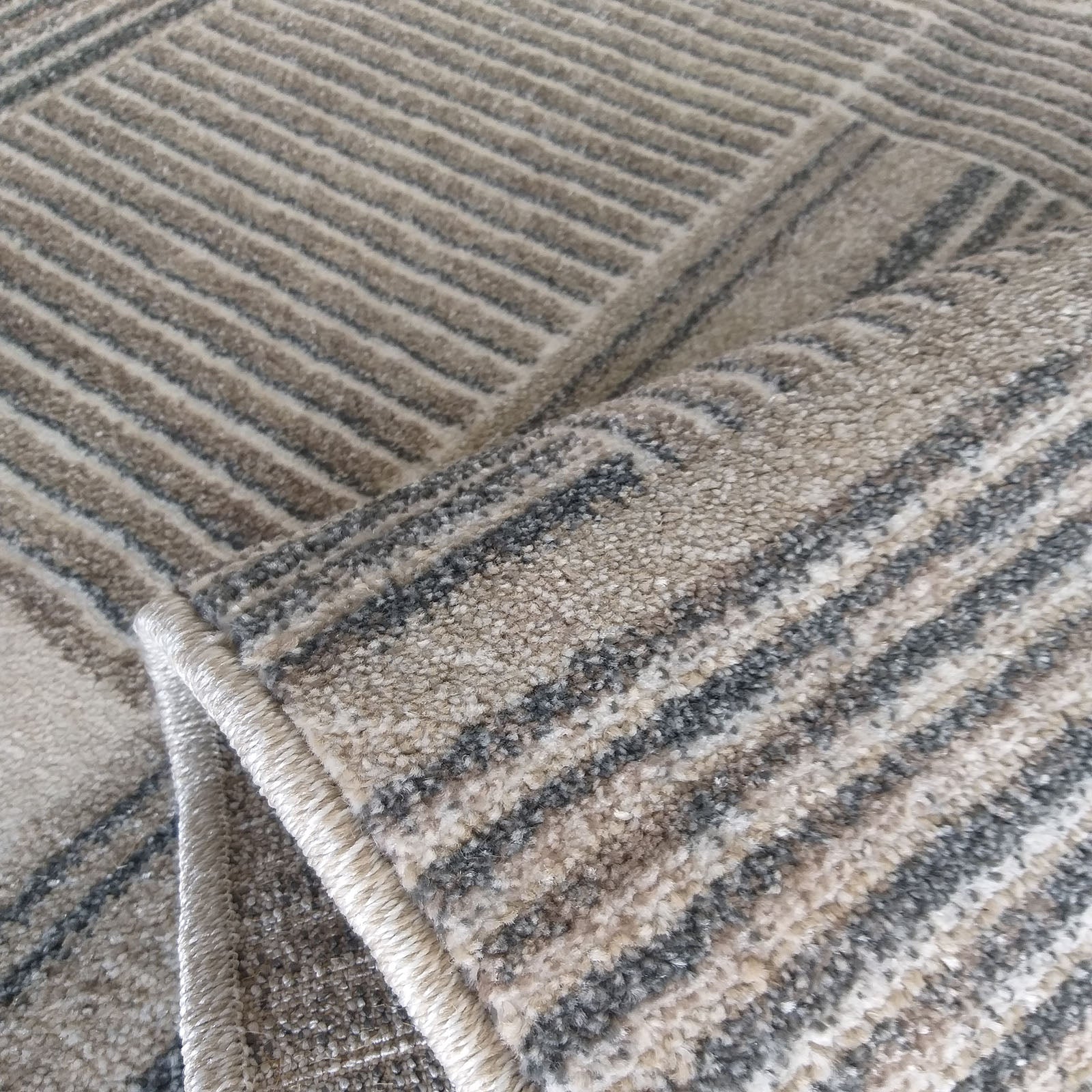 Tapis texturé aux motifs géométriques de rayures grises, beiges et plus claires, partiellement roulé