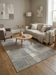 Tapis rectangulaire à motifs géométriques abstraits en bandes et blocs gris clairs, foncés et beiges, dans un salon