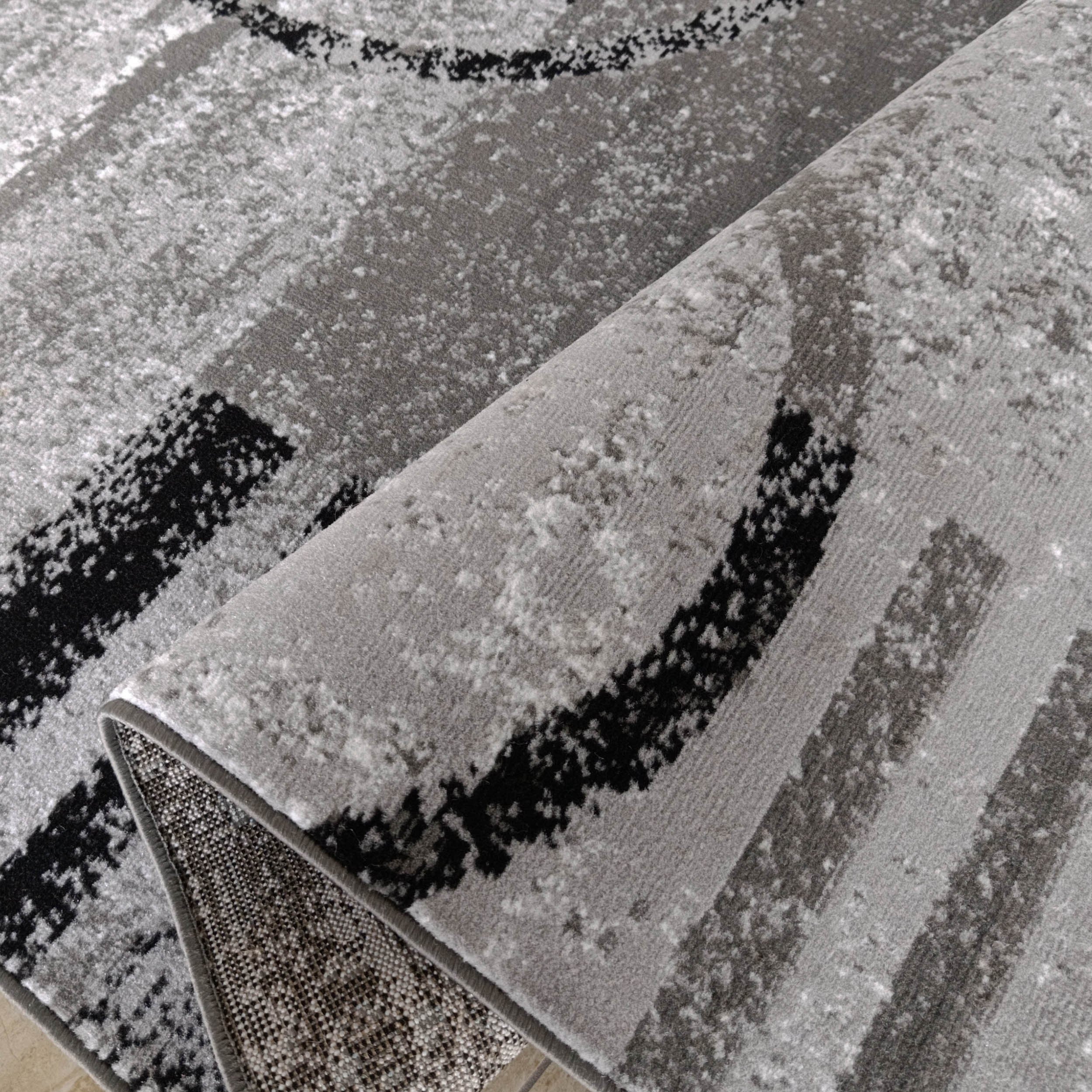 Tapis doux, gris, blanc et noir, motif rayé abstrait, partiellement roulé, montrant son envers tissé
