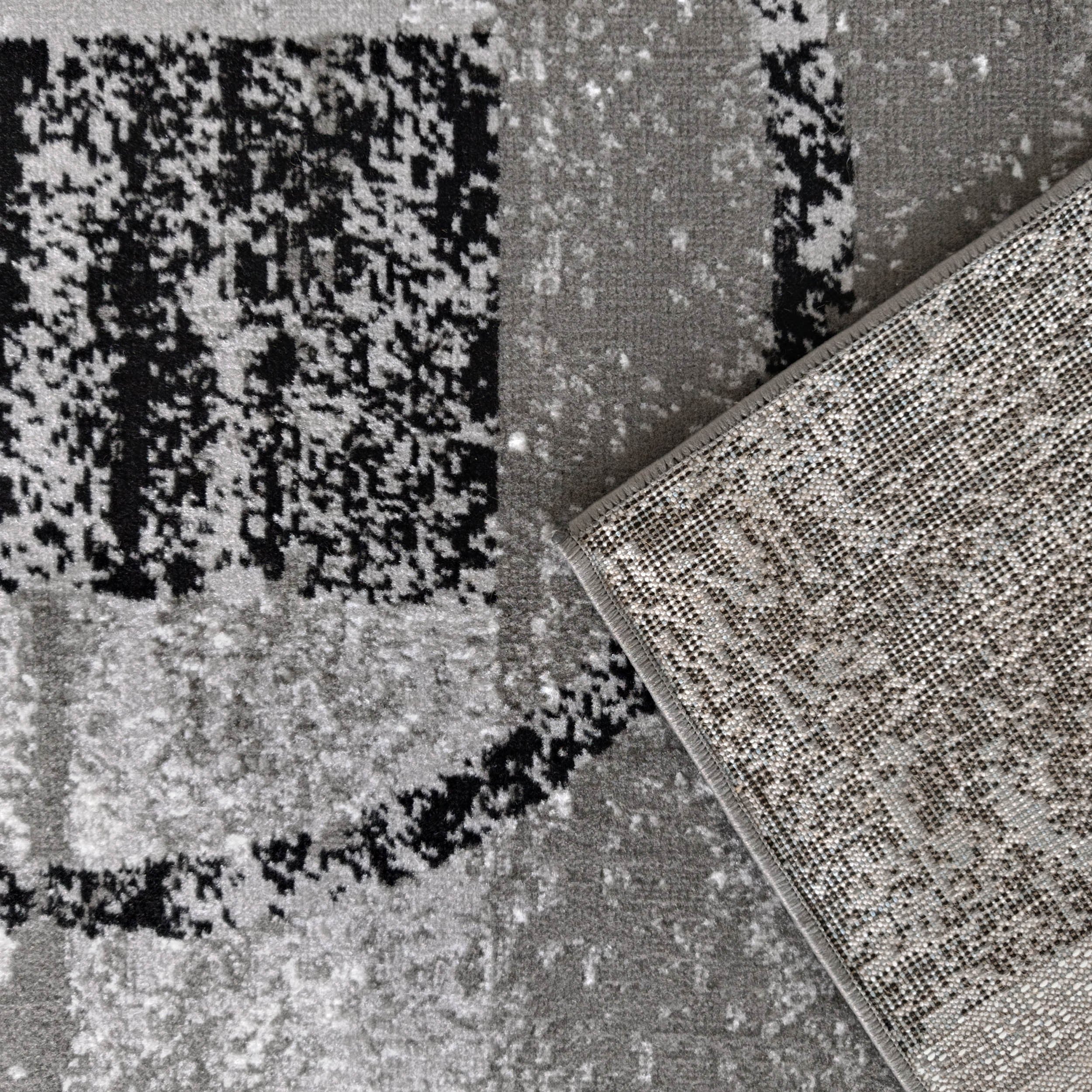 Tapis abstrait noir, gris clair et foncé avec un coin relevé dévoilant un envers gris à points noirs tissés