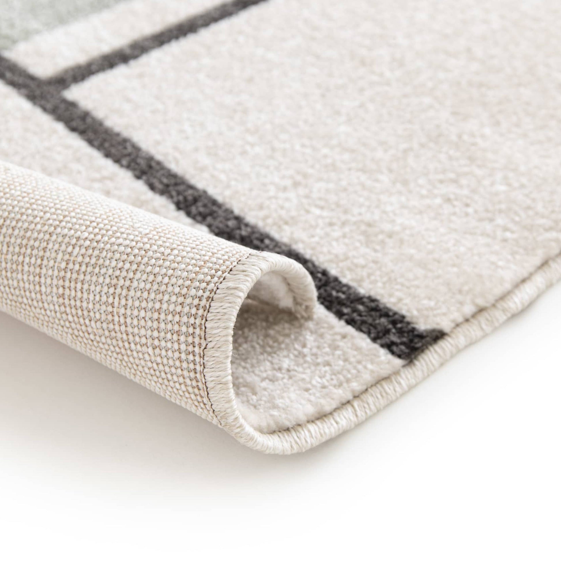 Tapis roulé beige clair avec des motifs géométriques gris foncé, révélant sa surface douce et son envers tissé