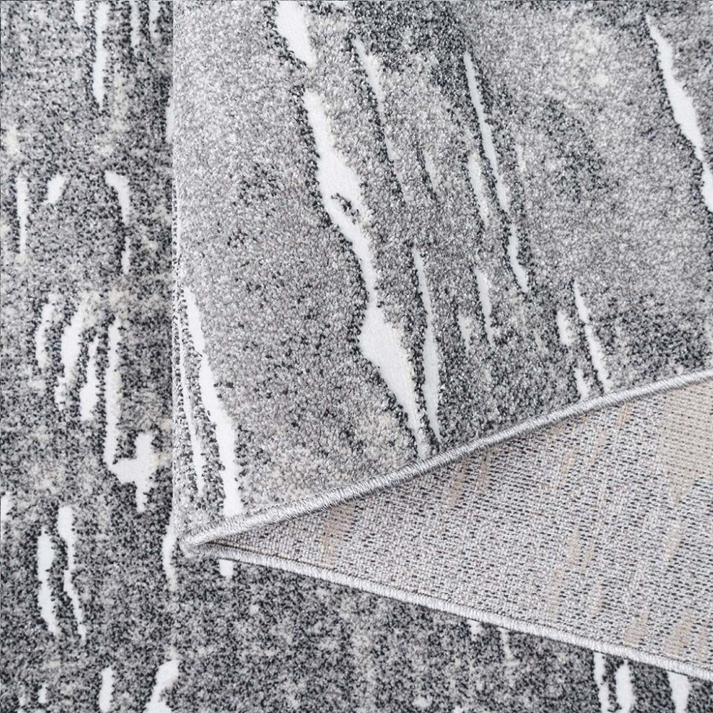 Tapis gris et blanc à motifs abstraits mouchetés avec une texture douce, plié pour montrer son envers tissé