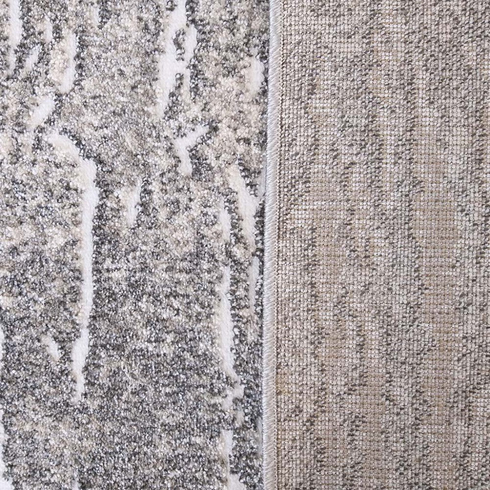 Tapis à la surface texturée, présentant des motifs abstraits gris et blancs, son envers tissé beige et gris est visible