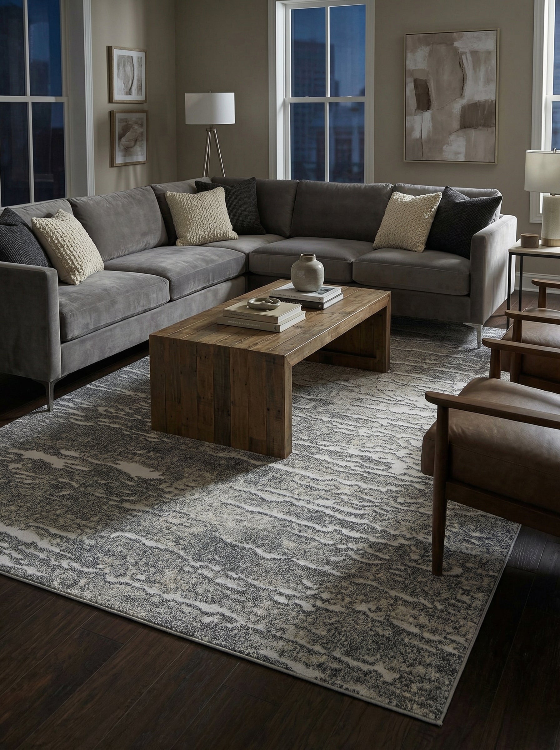 Tapis rectangulaire gris et crème avec un motif abstrait texturé, posé sur un sol en bois foncé dans un salon élégant