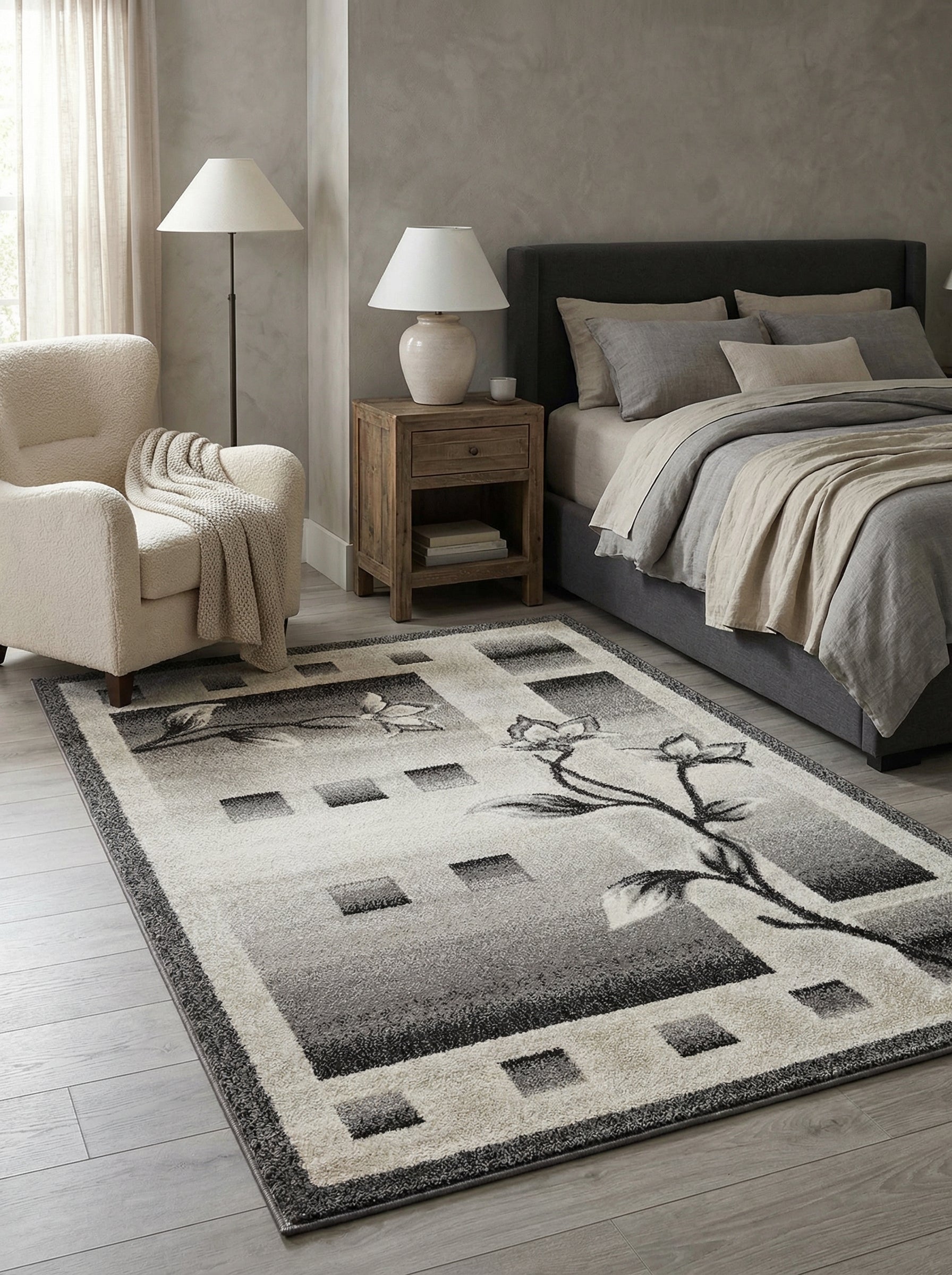 Tapis rectangulaire à motifs floraux et géométriques en dégradé de gris, crème et noir, posé sur sol clair d'une chambre