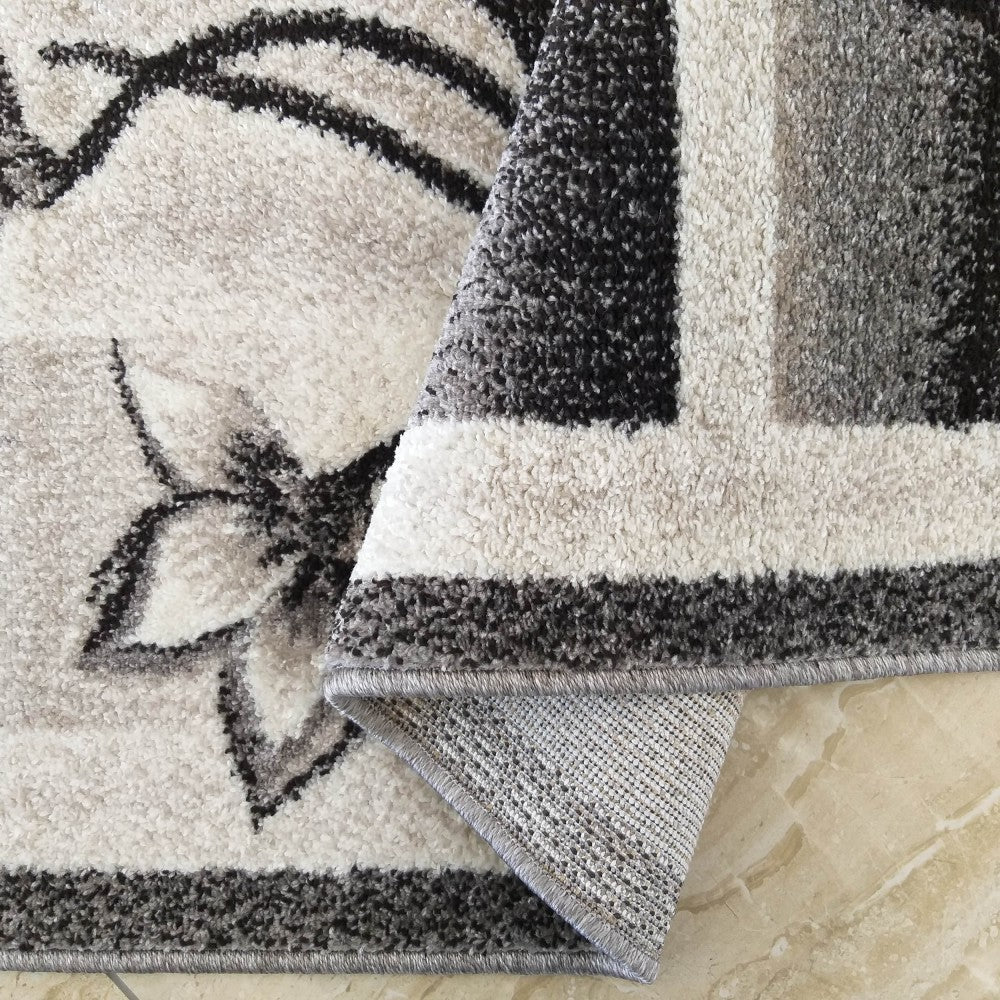Tapis moelleux aux motifs floraux noirs et gris sur fond blanc, plié pour révéler des bandes géométriques et son envers