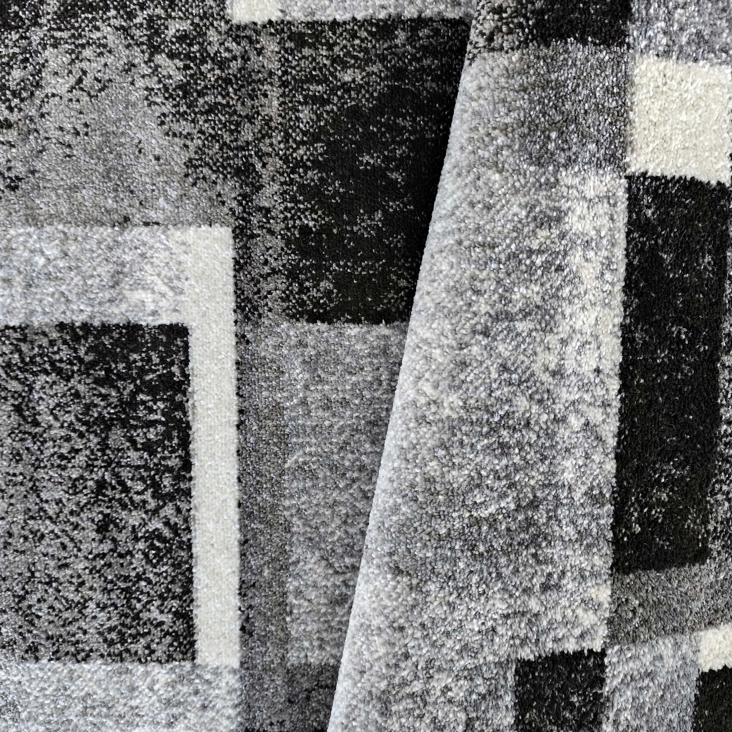 Gros plan sur un tapis texturé à motifs géométriques en carrés noirs, gris et blancs, avec une partie repliée
