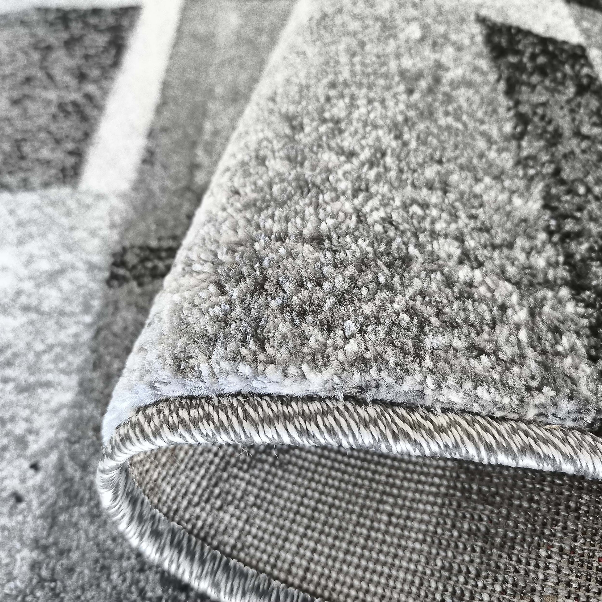 Tapis gris à motifs géométriques en gros plan, montrant le poil texturé, le bord ourlé et le revers tissé
