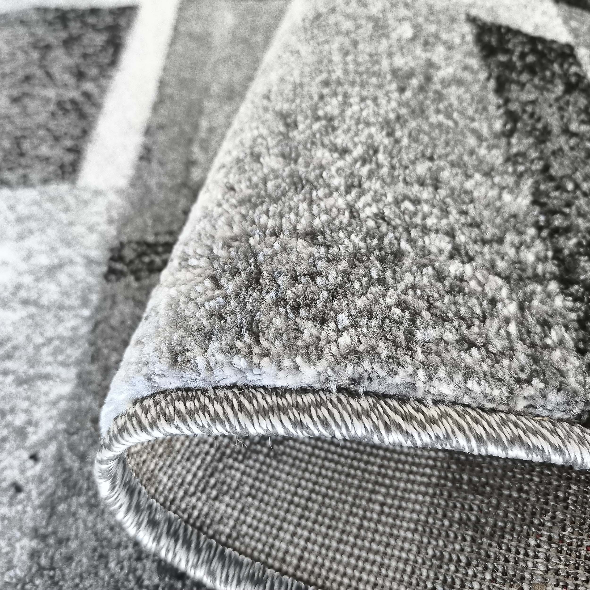 Tapis gris à motifs géométriques en gros plan, montrant le poil texturé, le bord ourlé et le revers tissé