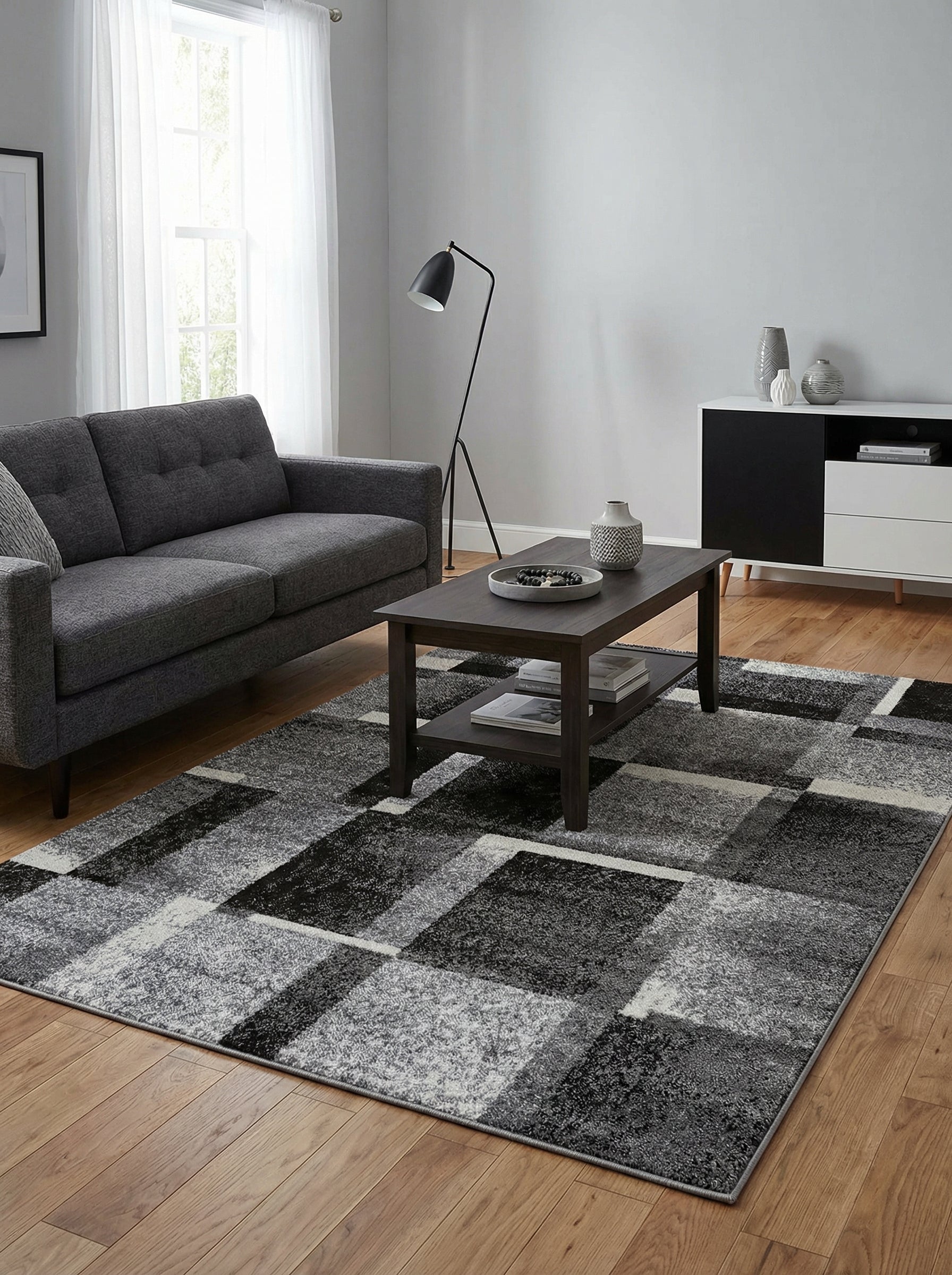 Grand tapis rectangulaire aux motifs géométriques abstraits en blocs de gris, noir et blanc cassé, dans un salon