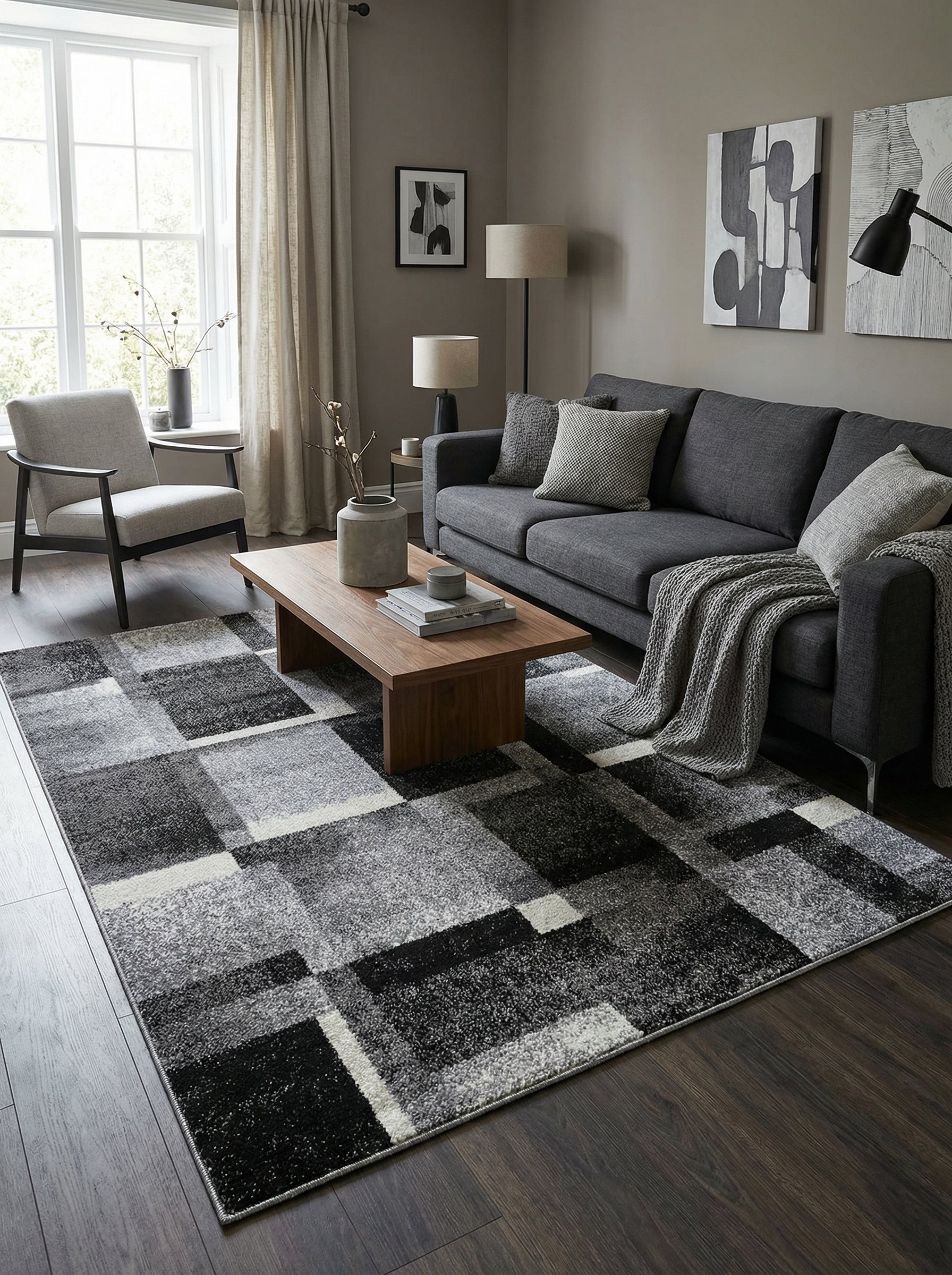 Tapis rectangulaire à motifs géométriques abstraits en blocs noir, gris et blanc, posé sur un parquet sombre dans un salon moderne