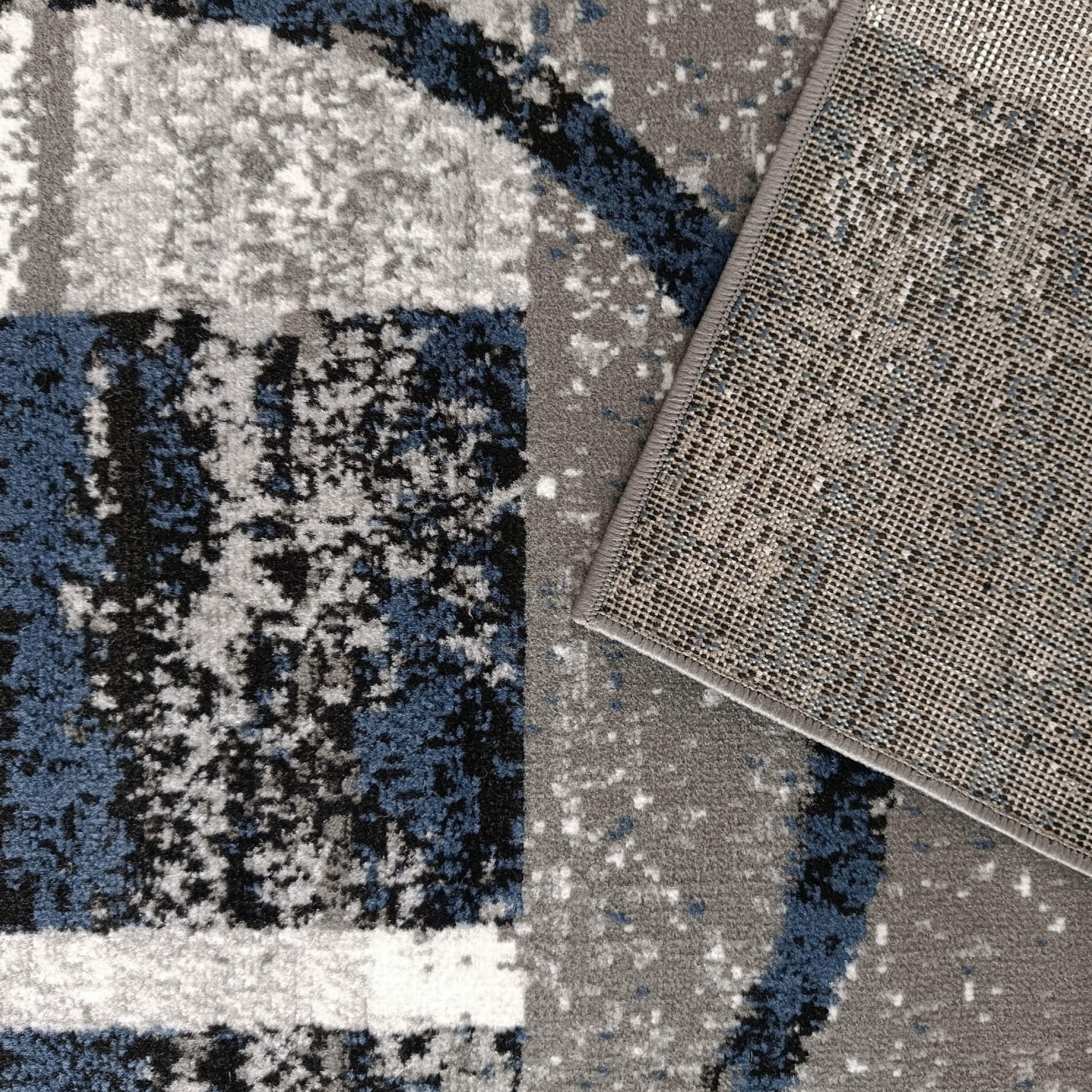 Tapis moelleux aux motifs abstraits gris, blancs, noirs et bleus intenses, avec le dessous en toile tissée visible