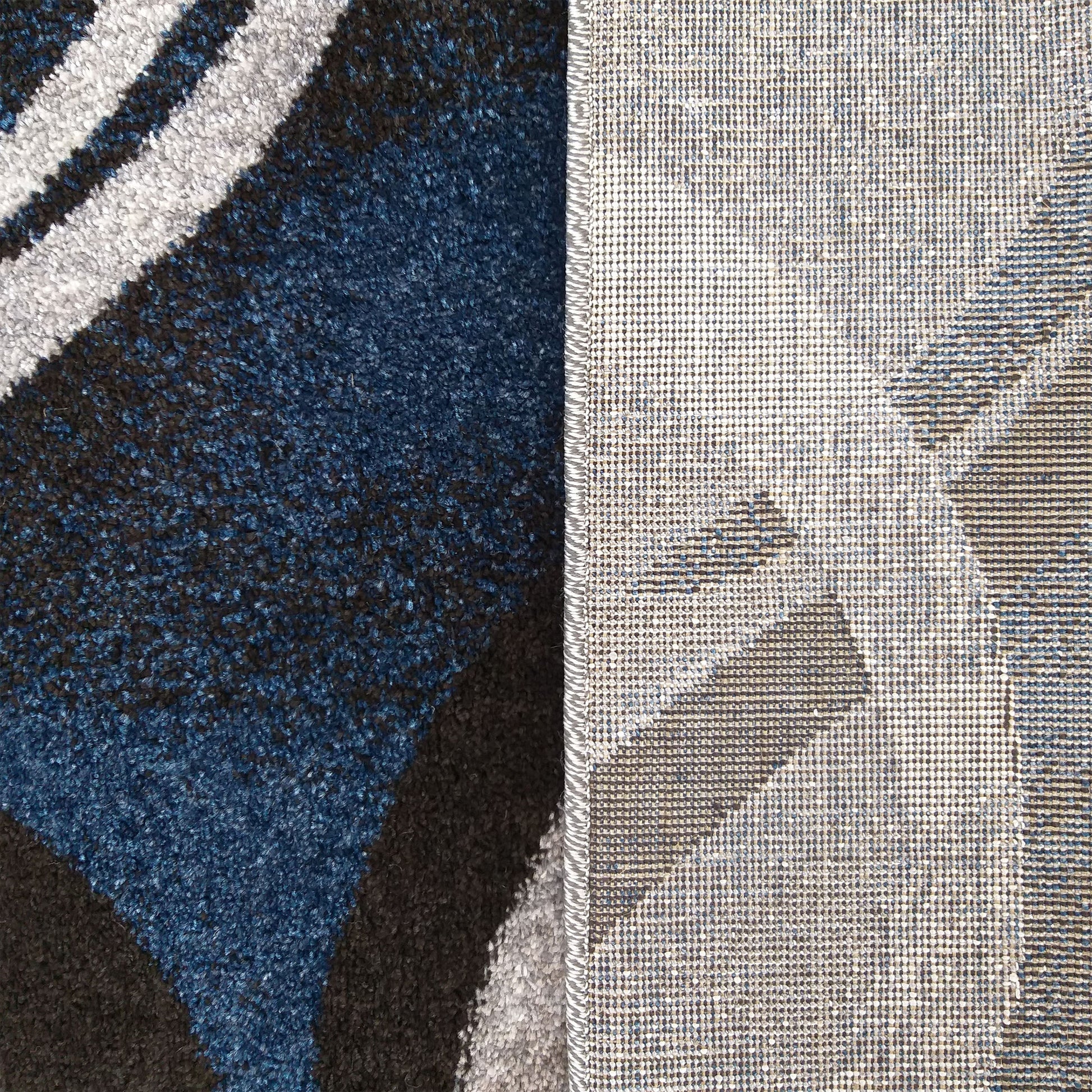 Tapis montrant sa face supérieure velue aux motifs abstraits bleus, gris et noirs, et son envers tissé en maille serrée avec bordure