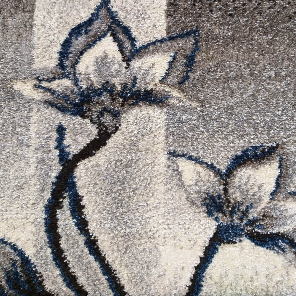 Tapis à texture moelleuse avec des motifs floraux stylisés bleu foncé, noir et crème sur un fond rayé gris varié
