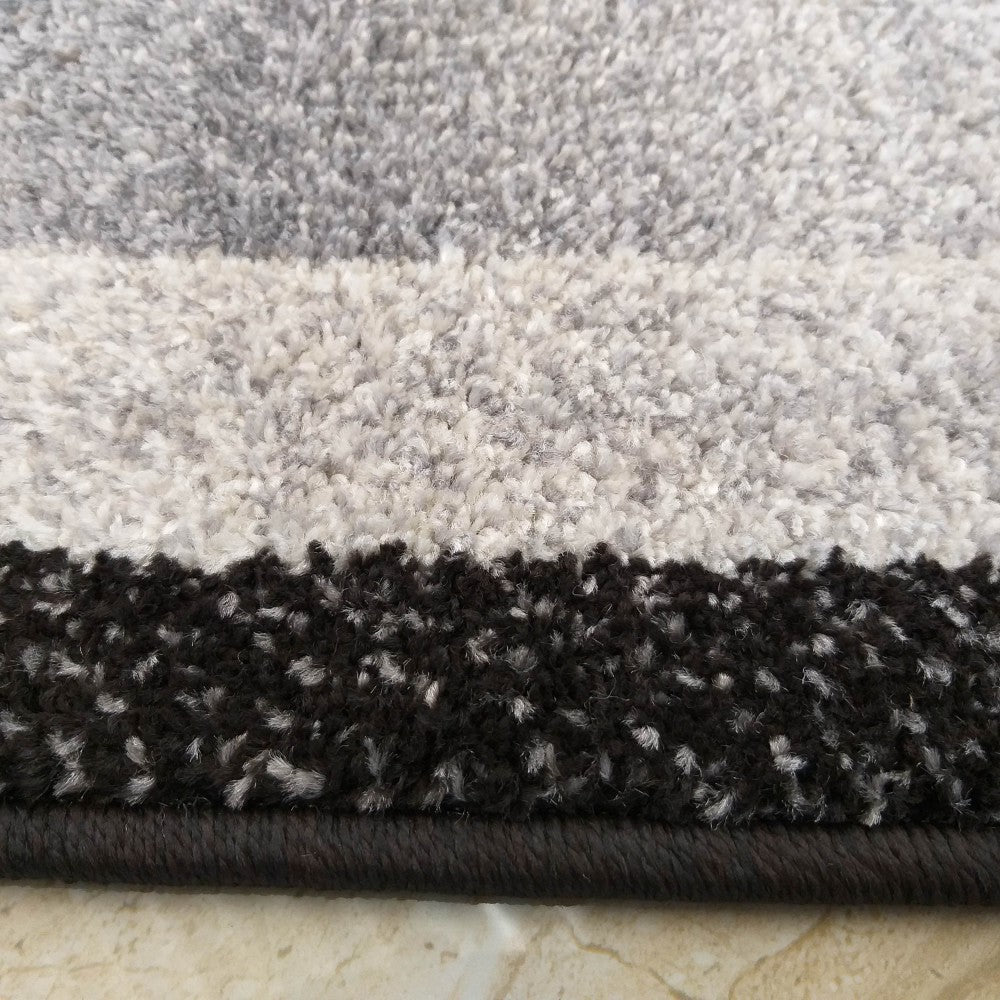 Gros plan sur un tapis texturé à bandes horizontales de gris clair, gris moyen et noir, avec une bordure tissée foncée