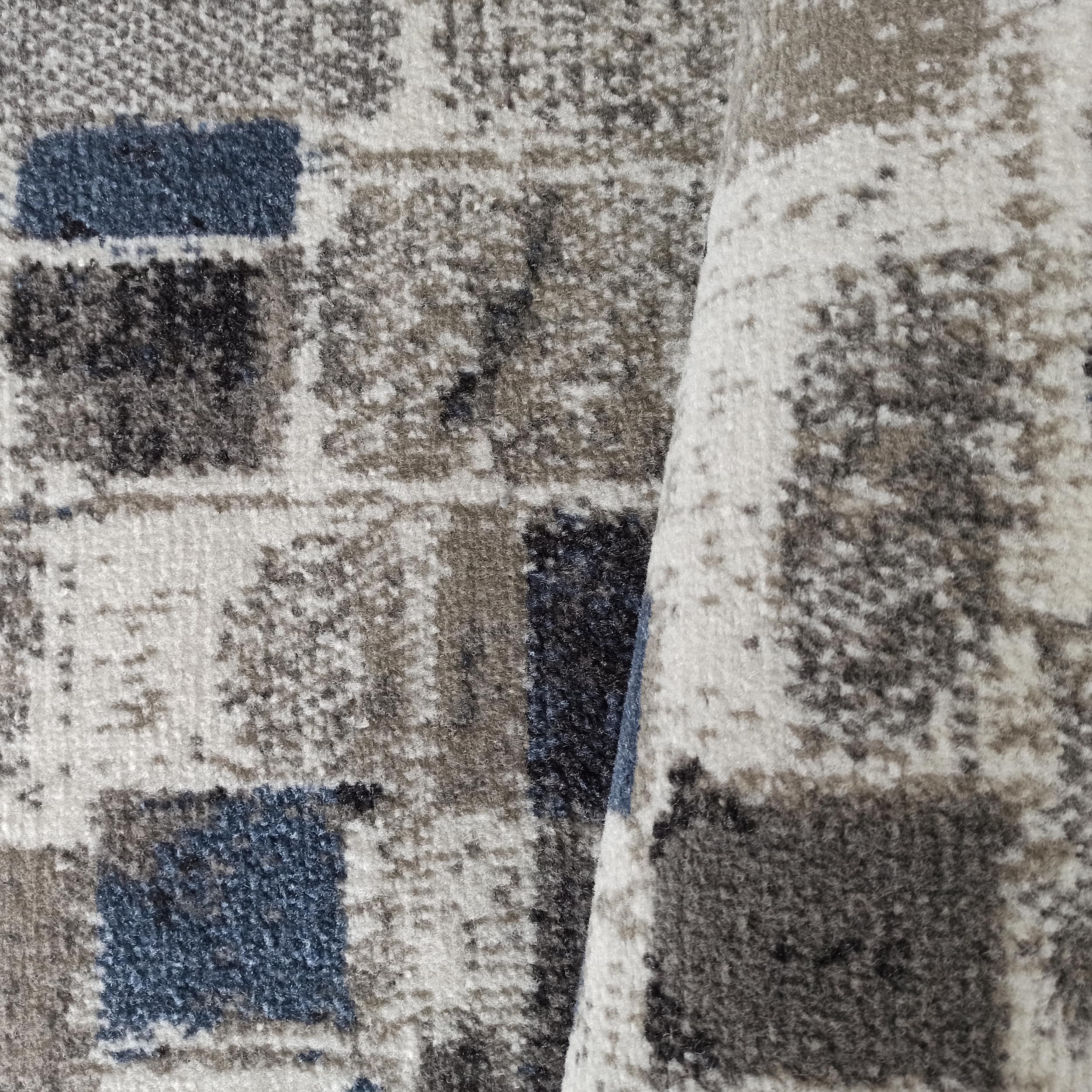 Tapis aux motifs de blocs abstraits variés gris, blancs et bleus foncés, avec une partie du tapis roulée sur la droite