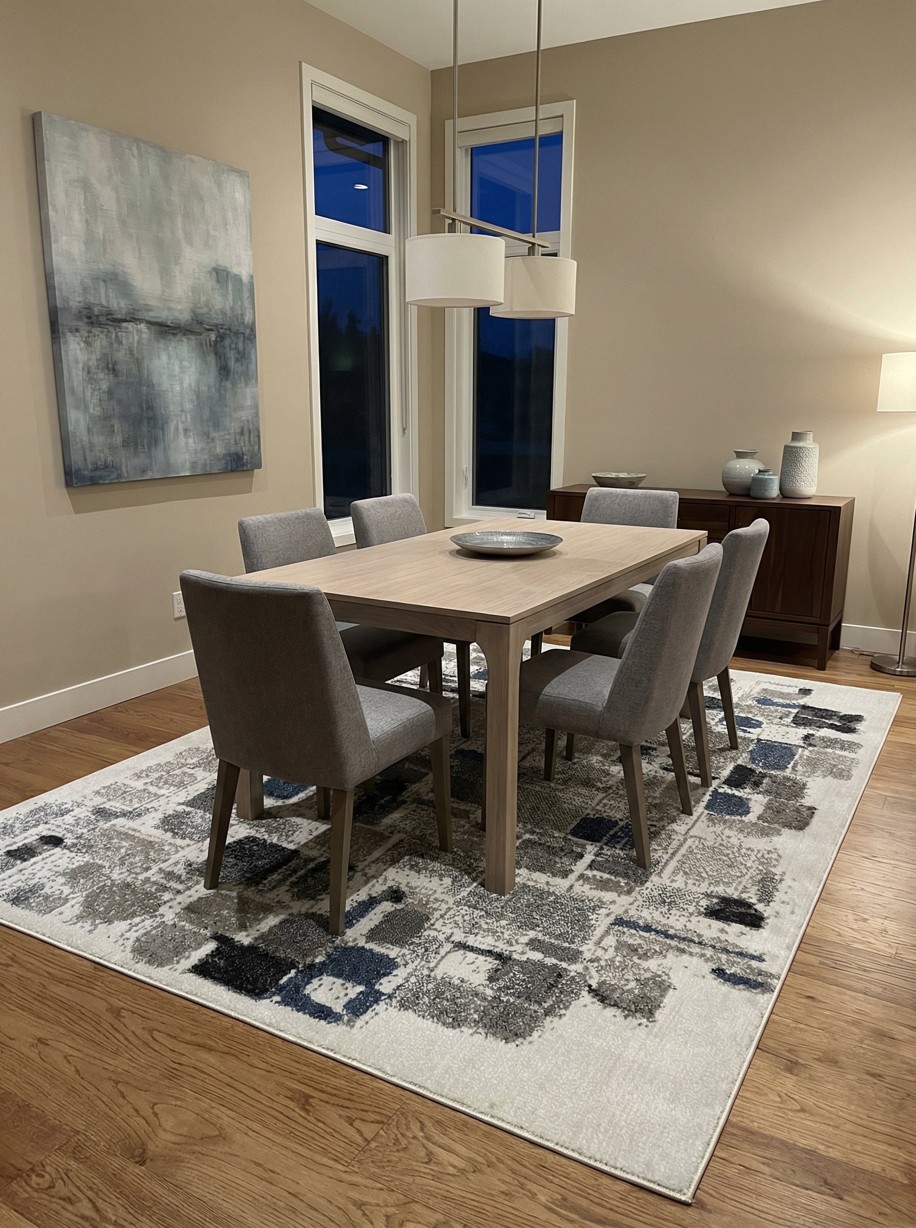 Tapis rectangulaire aux motifs abstraits gris, noirs et bleus sur fond blanc cassé, en fibres tissées, posé sous une table de salle à manger
