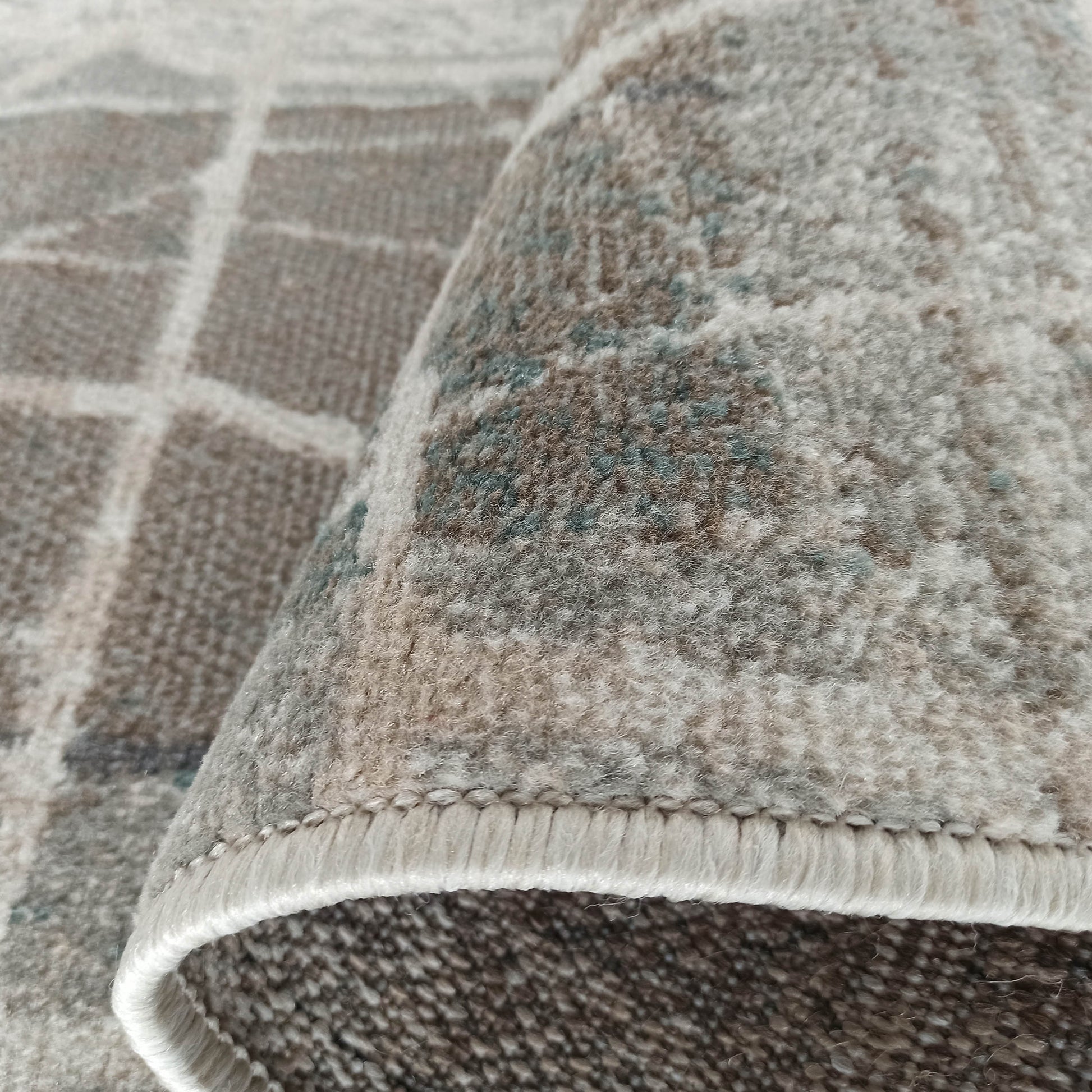 Tapis texturé enroulé, affichant un motif quadrillé beige et gris sur la partie plane et un mélange flou de brun, beige et bleu sur la surface moelleuse