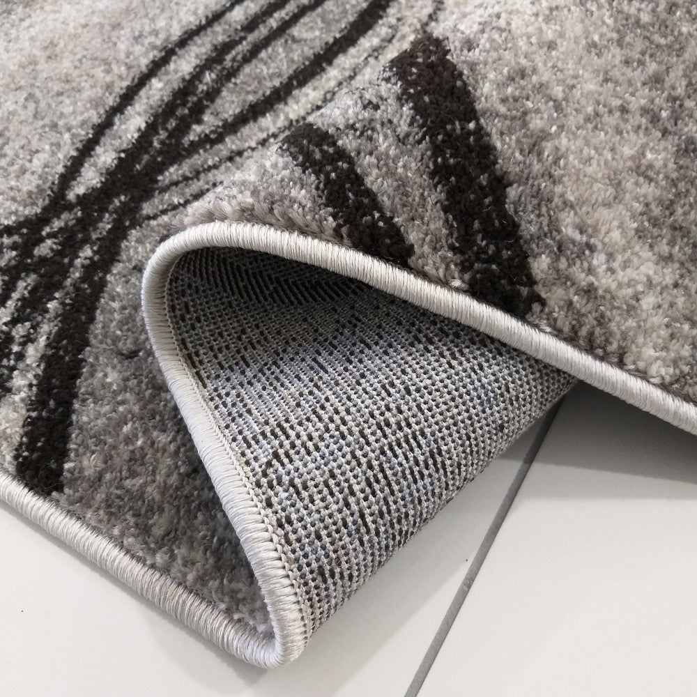 Gros plan sur un tapis gris chiné à motifs abstraits noirs. Une section est repliée, révélant son envers texturé gris clair et foncé