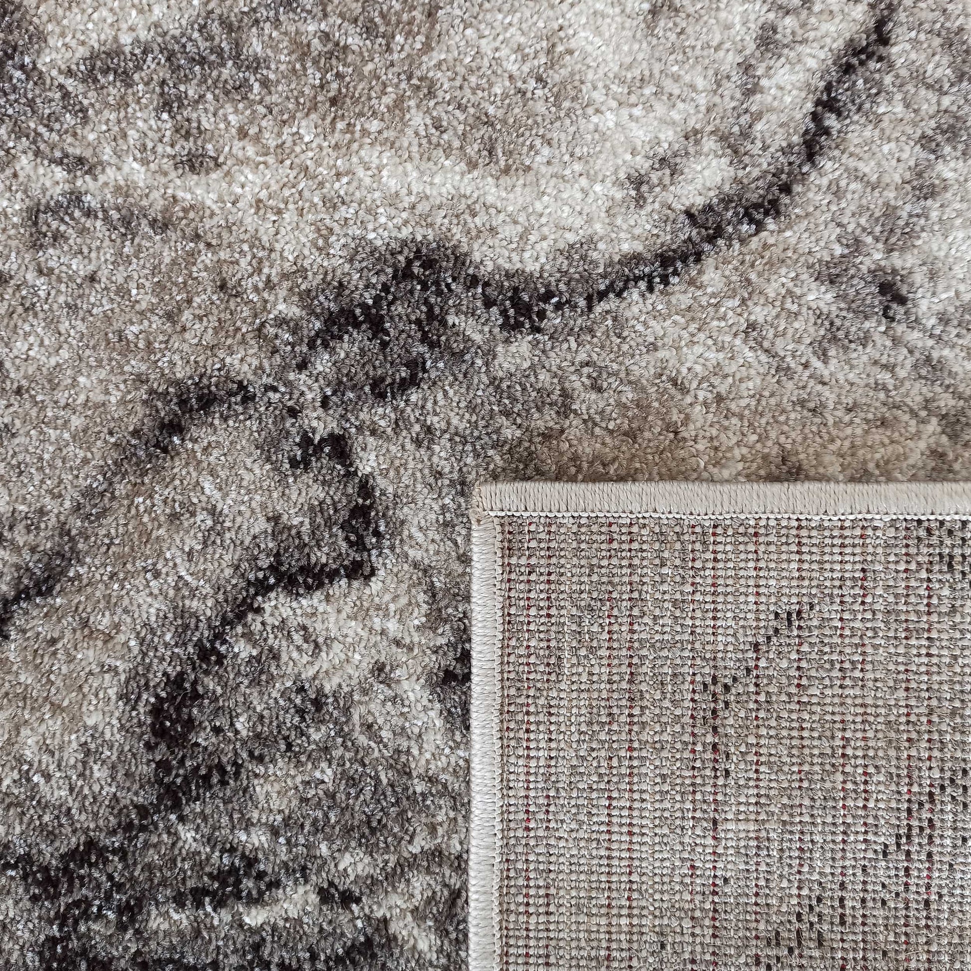 Tapis à poils courts aux motifs marbrés de gris, beige et marron. Le coin révèle un envers tissé à trame rouge